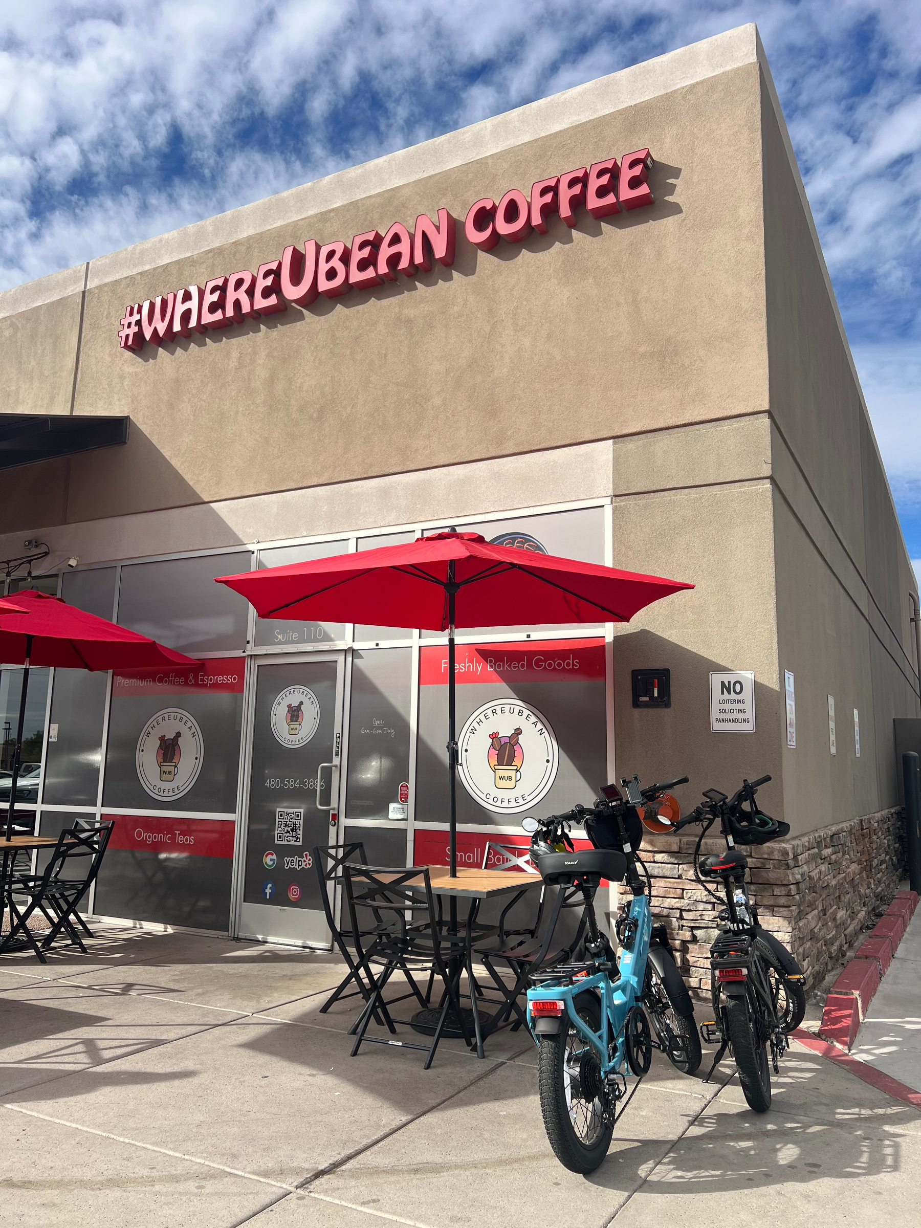 A coffee shop with red umbrellas and bicycles parked outside.