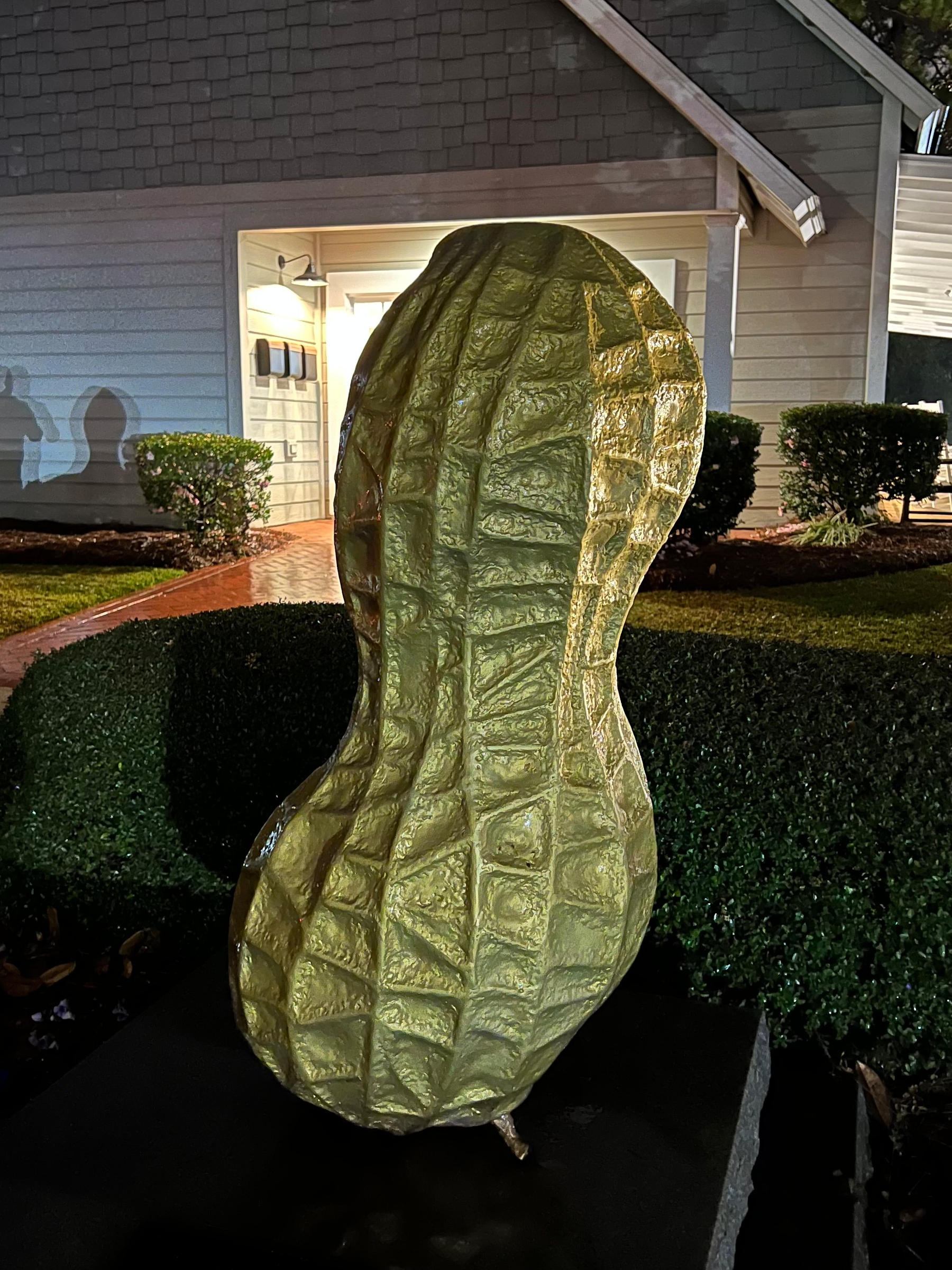 A large, golden peanut sculpture is displayed outdoors in front of a building, surrounded by neatly trimmed bushes.