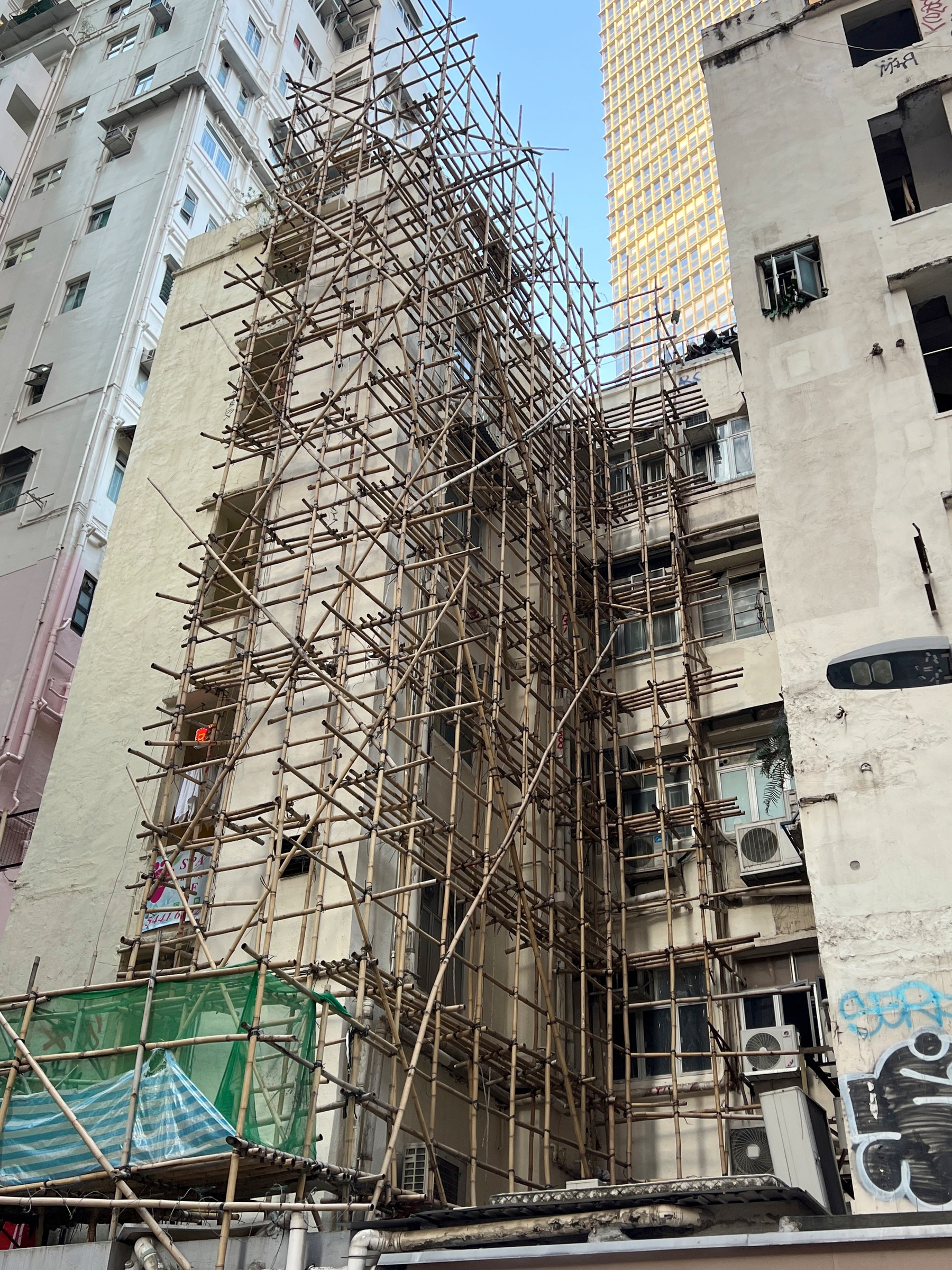 A building under construction or renovation is surrounded by bamboo scaffolding in an urban setting.