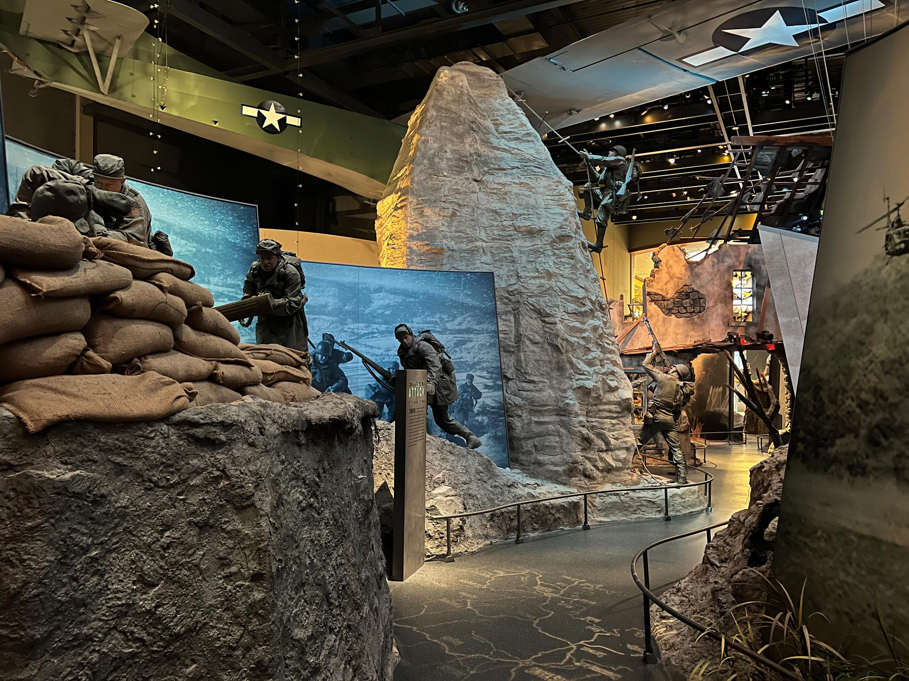 A museum exhibit displays detailed dioramas of soldiers in a wartime setting with sandbags and mountainous terrain.