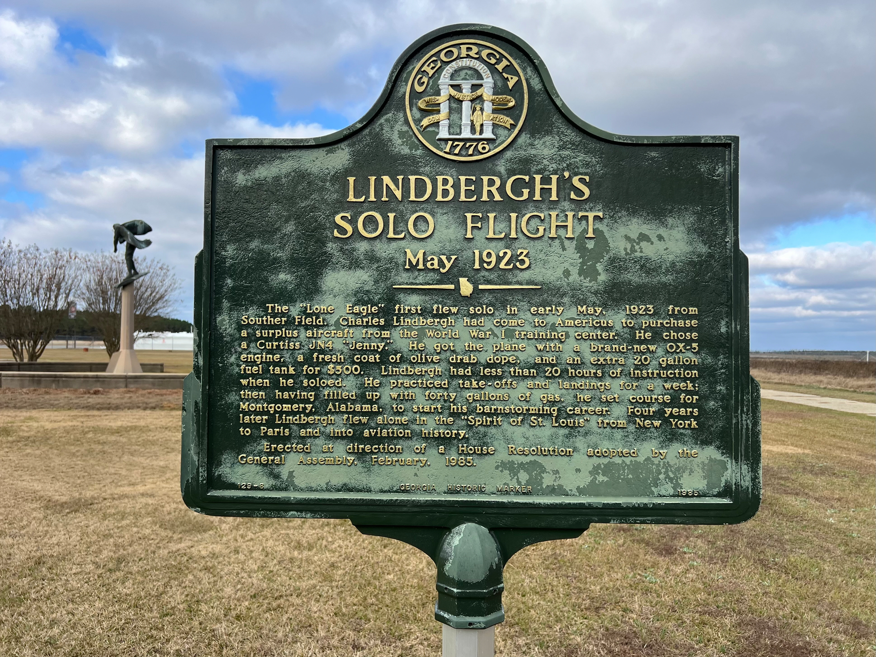 A historical marker commemorates Charles Lindbergh's solo flight in May 1923, featuring text detailing the event, with a grassy field and cloudy sky in the background.
