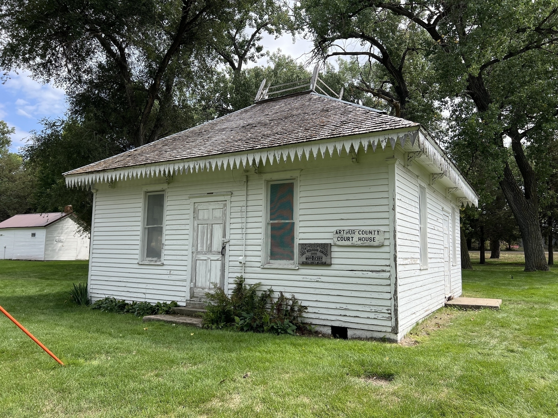 A small, white, historical building labeled "Arthur County Court House" sits surrounded by grass and trees.