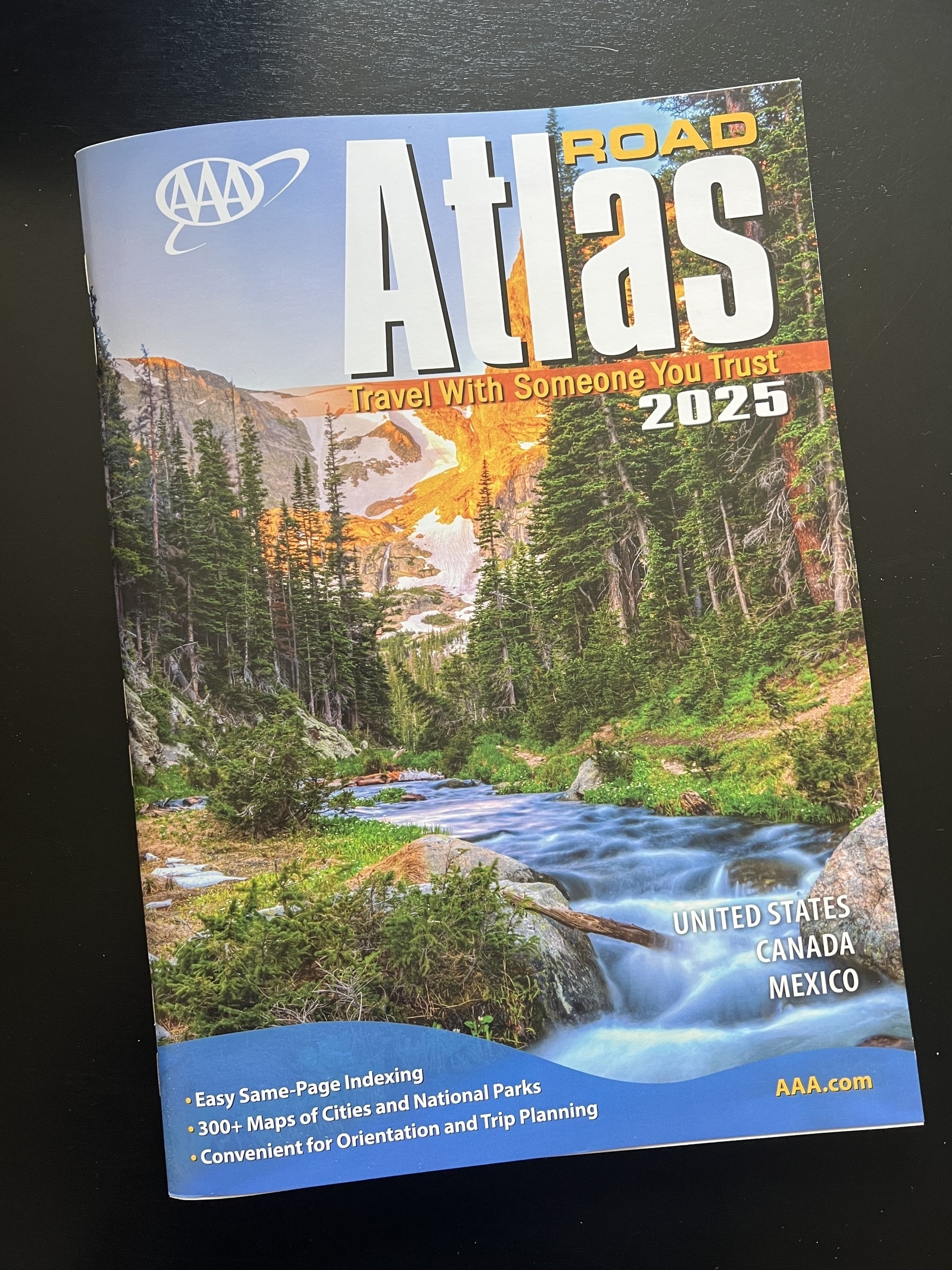 A 2025 road atlas cover features a scenic mountain landscape with a flowing river and trees, along with maps for the United States, Canada, and Mexico.