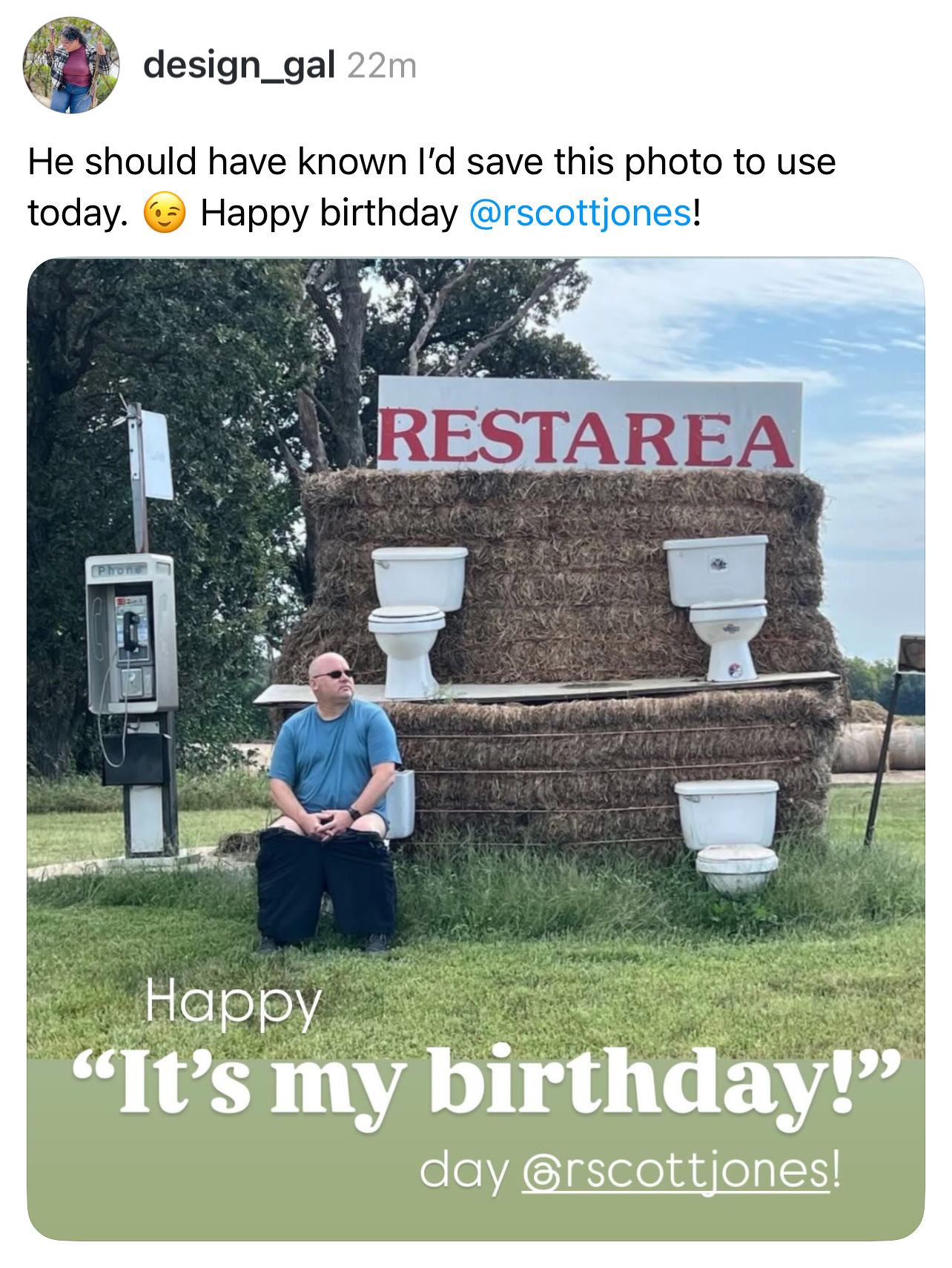 A man is sitting in front of a humorous restroom-themed display made of hay bales and toilets, with a sign reading RESTAREA.