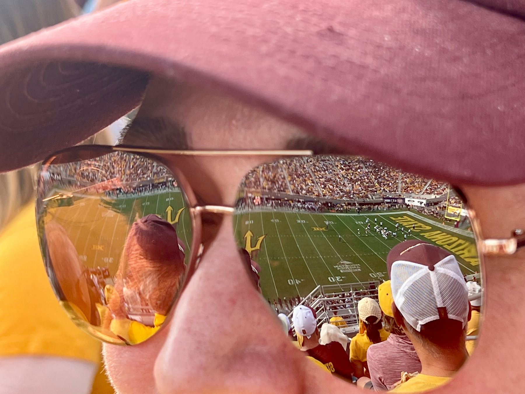 Reflected in sunglasses, a stadium filled with spectators is seen watching a football game.