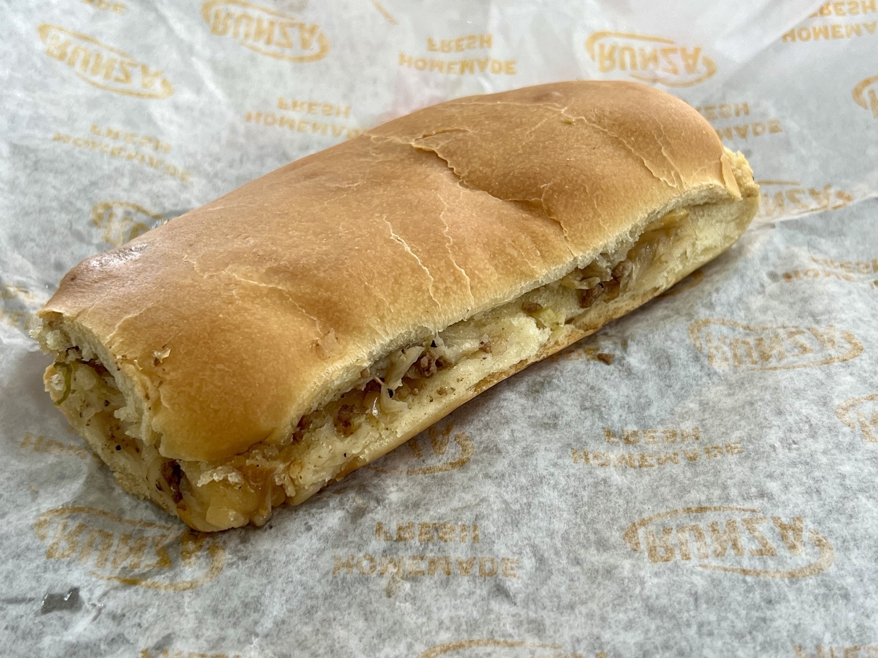 A toasted sandwich filled with cheese and perhaps some meat ingredients is displayed on branded paper.