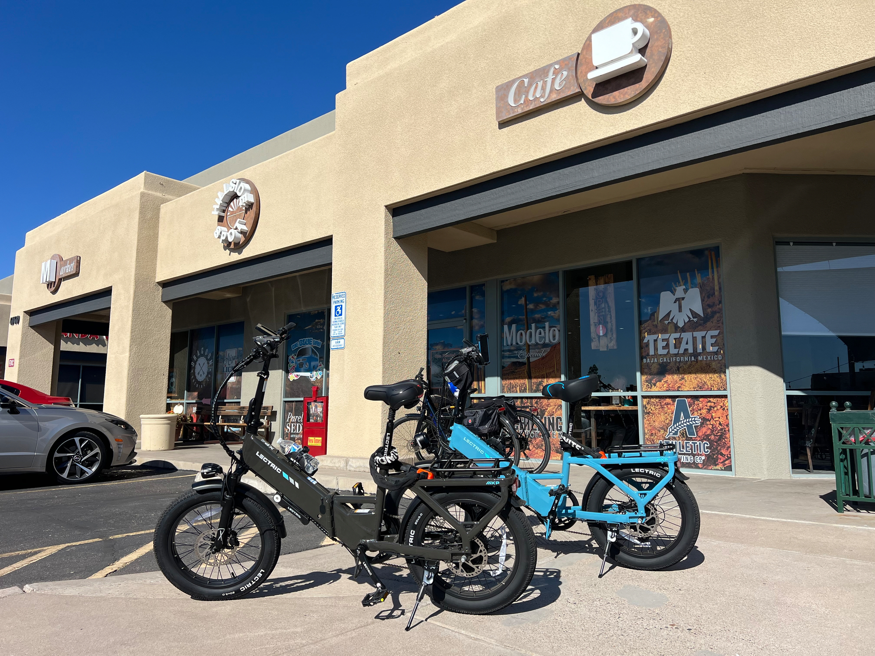Two bikes are parked in front of a cafΓ© with a beige exterior and several advertisements on the windows.