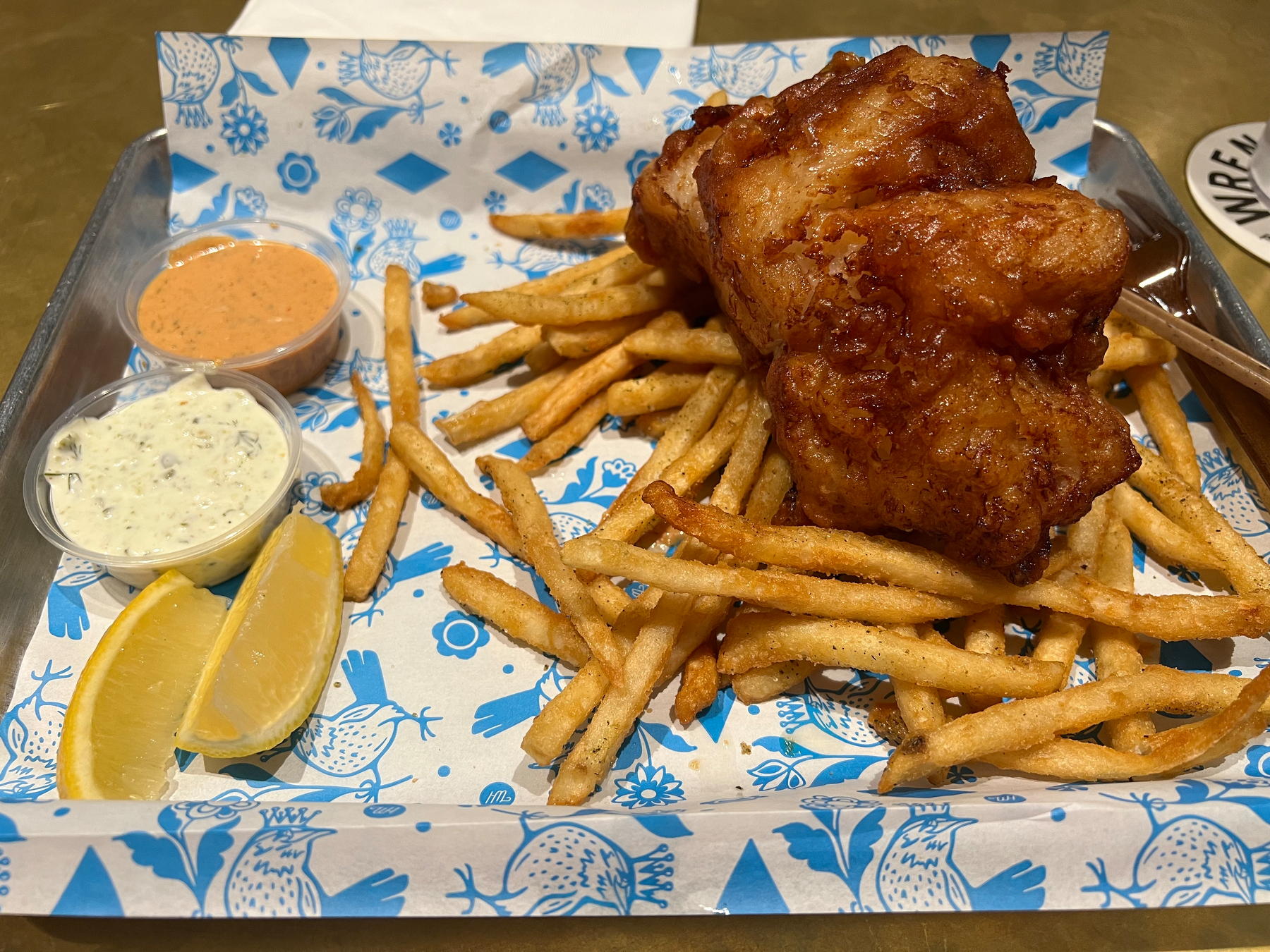 Golden fries and fried fish are served on a decorative tray with lemon wedges and two dipping sauces.
