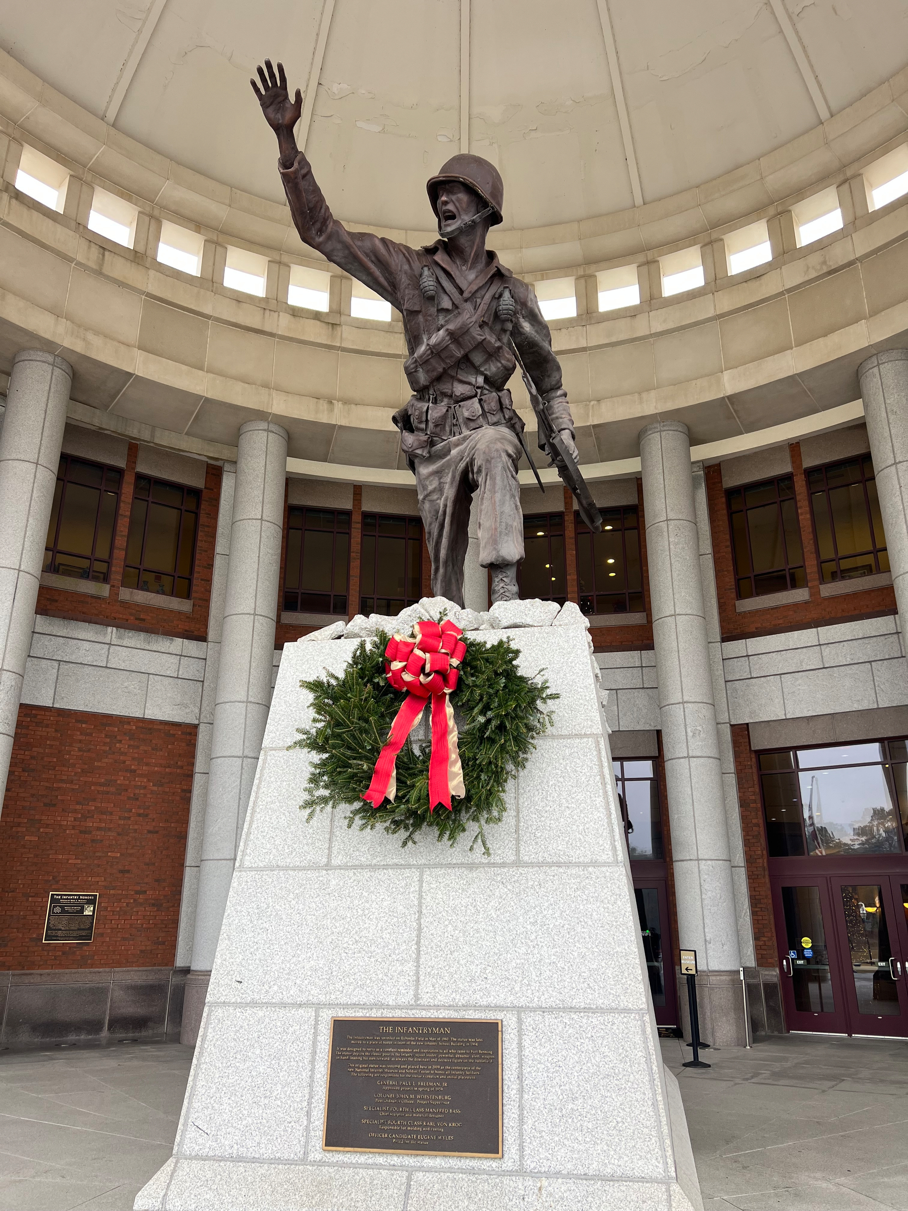 A statue of a soldier in a dynamic pose stands on a pedestal, adorned with a wreath and red ribbon.