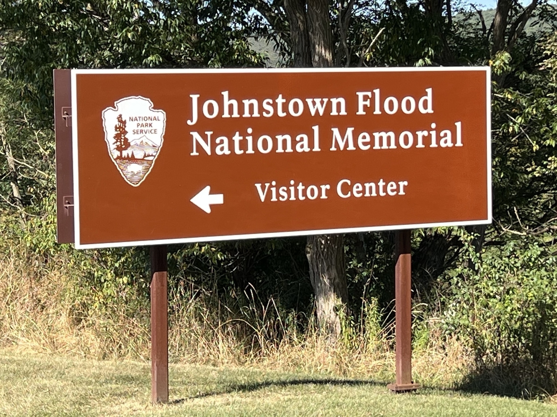 A historical information sign overlooks a scenic landscape with a house and rolling hills in the background.