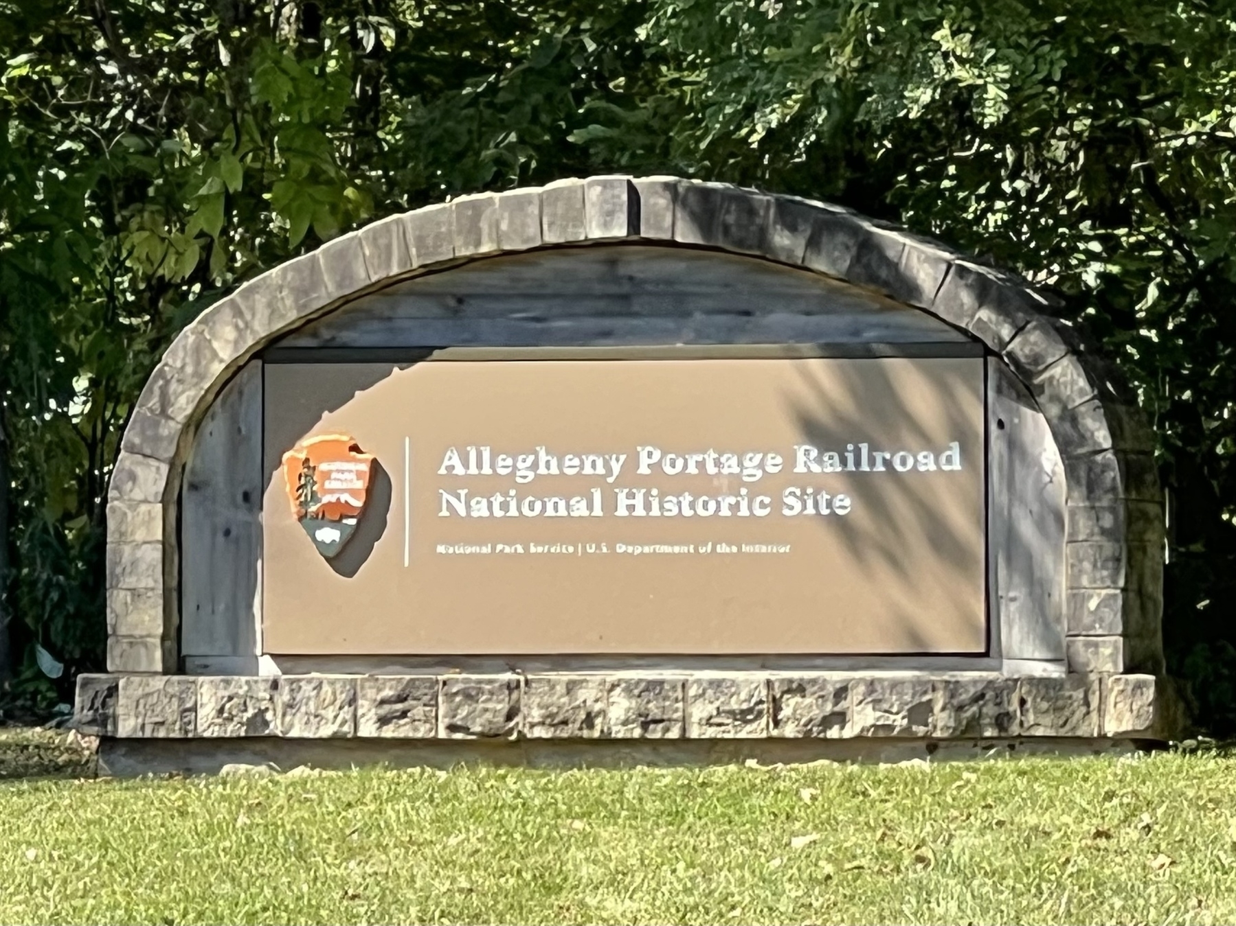 A sign for the Allegheny Portage Railroad National Historic Site is displayed outdoors, surrounded by greenery.