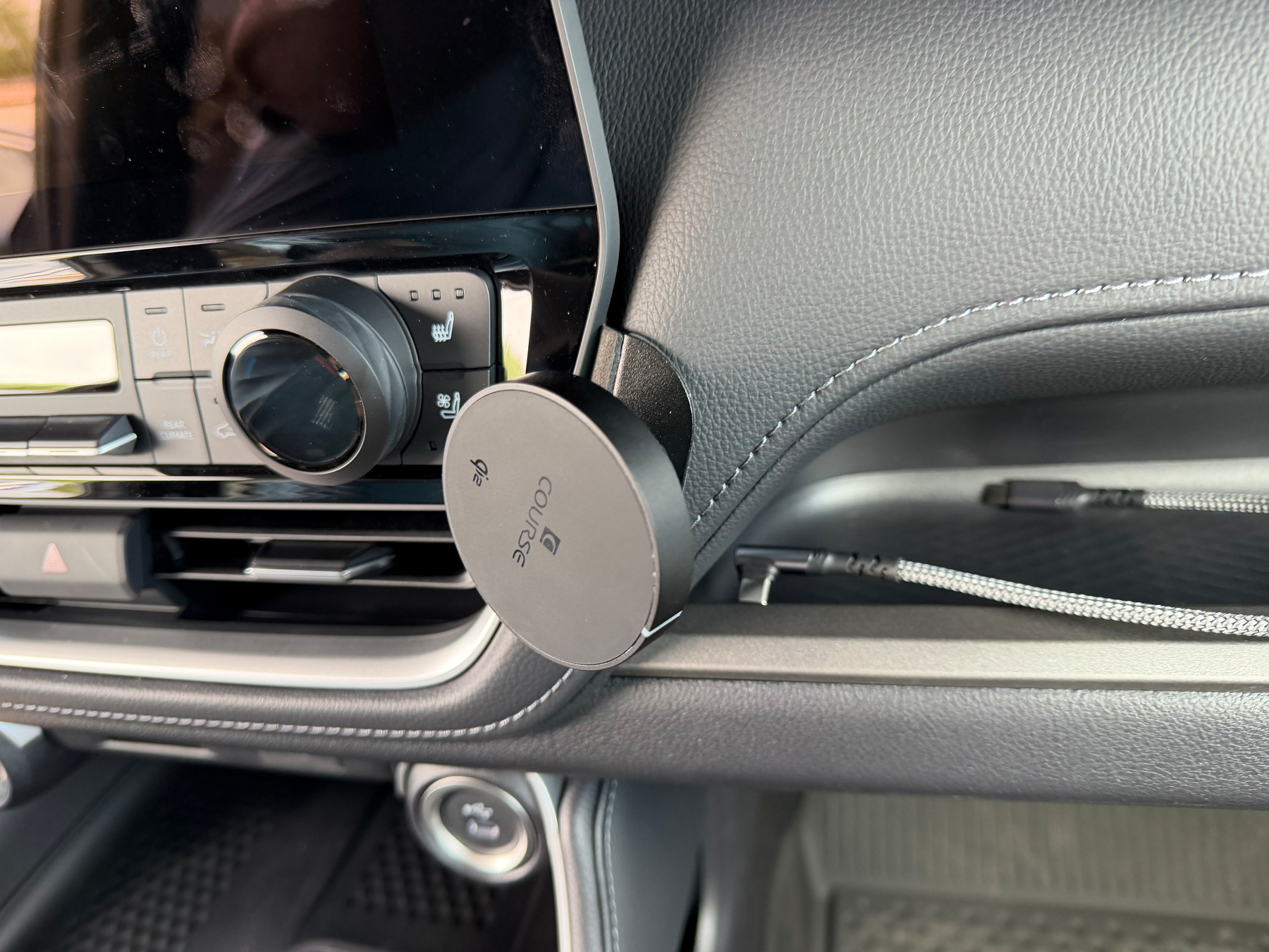 A magnetic phone holder is attached to the dashboard of a car near the control panel.