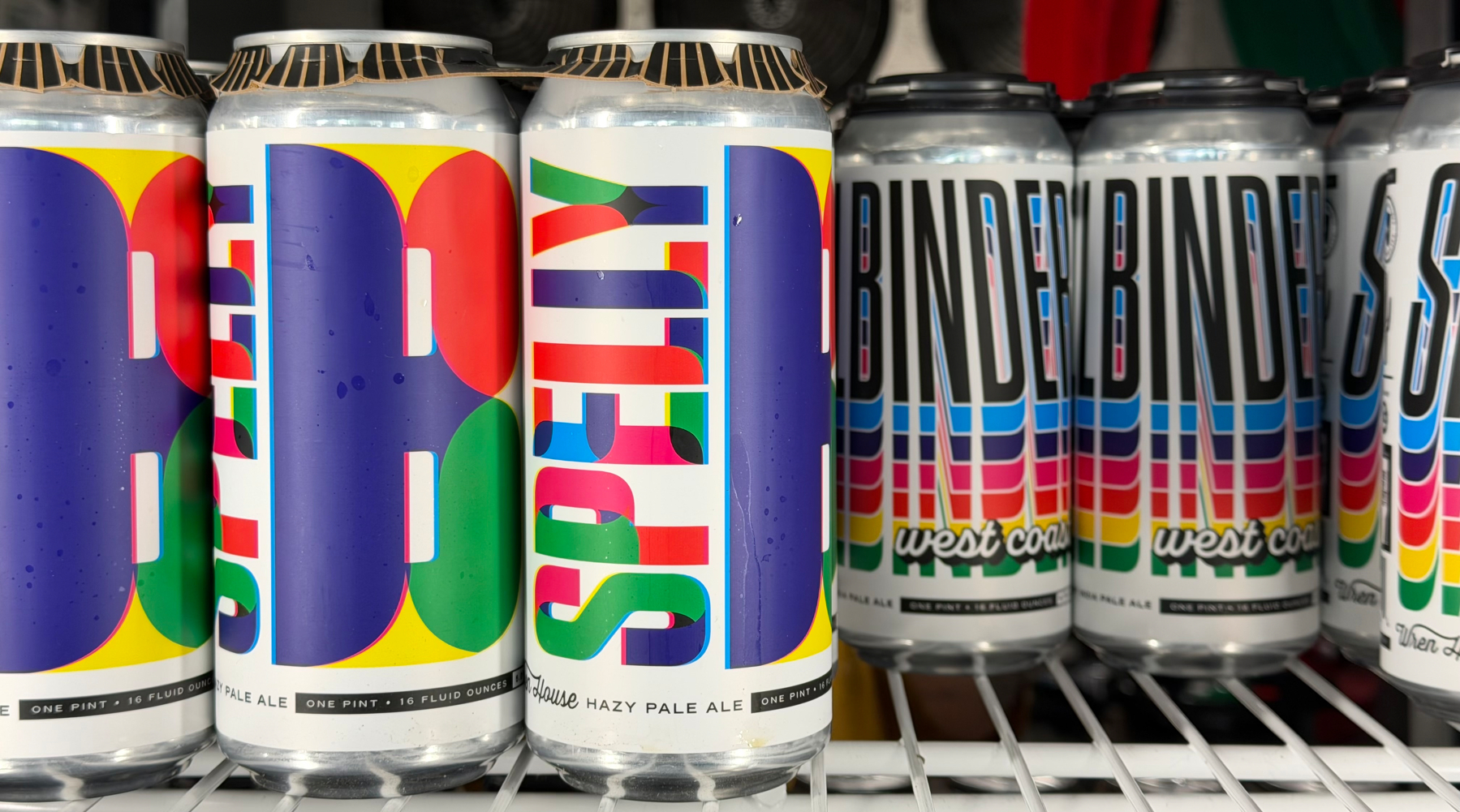 Brightly colored cans of craft beer with bold, artistic labels are displayed on a shelf.