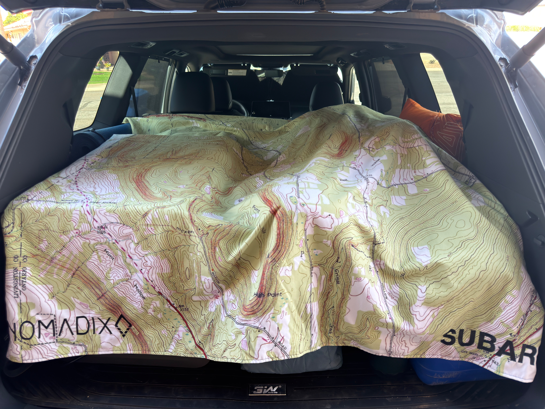 A topographic-patterned blanket with the words NOMADIX and SUBARU is spread out in the trunk area of a vehicle.