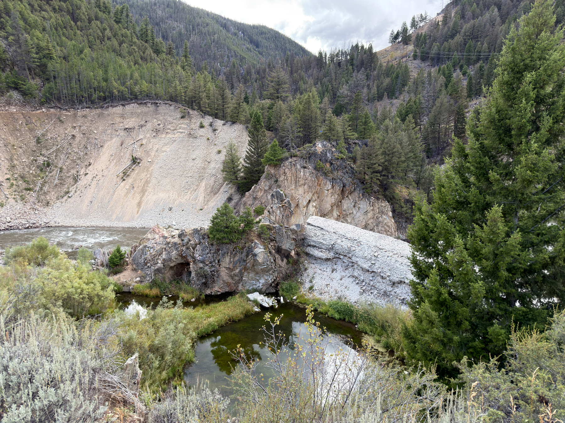 A river flows through a mountainous forested area featuring a natural rock arch over the water.