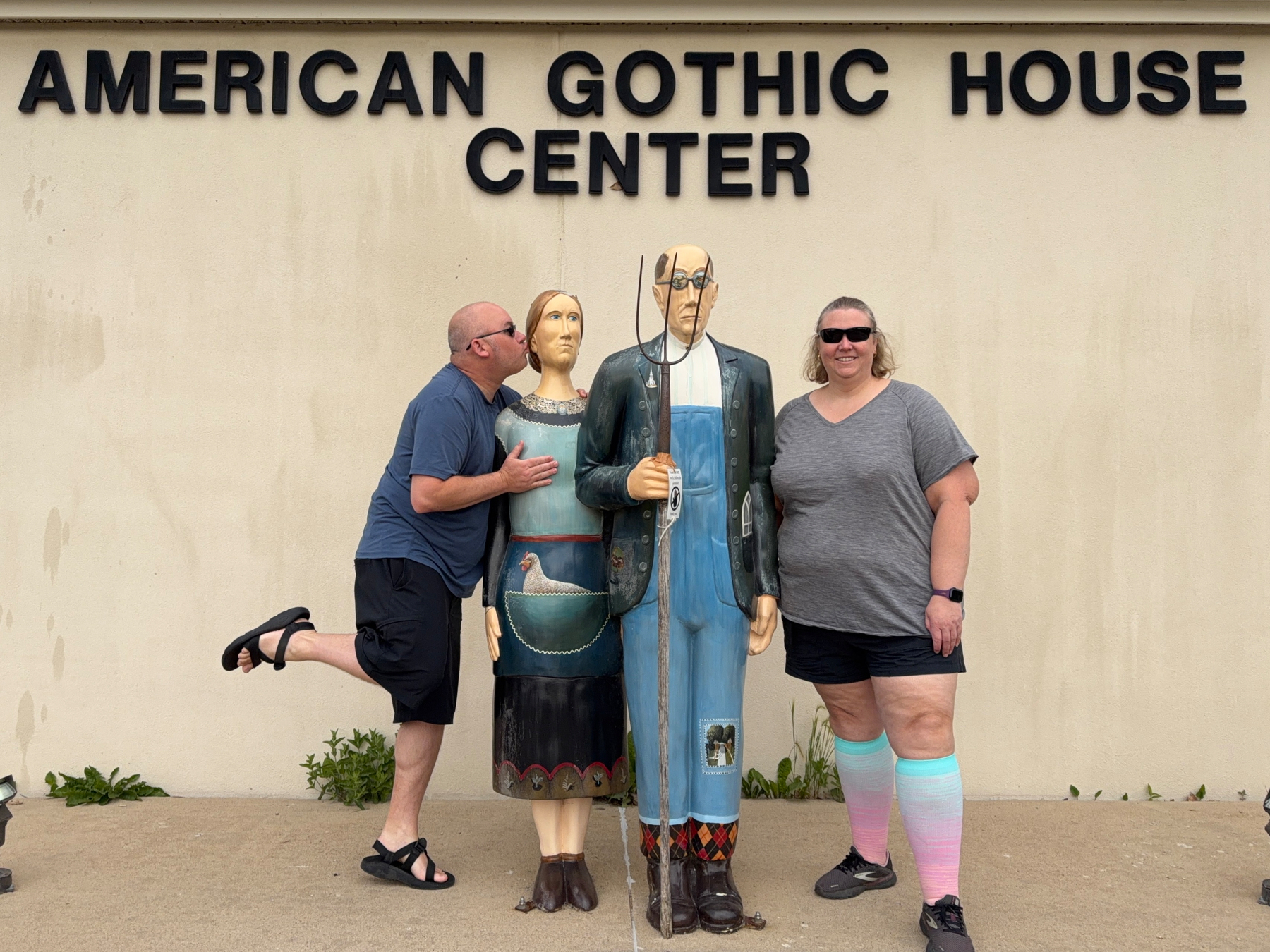 Two people pose humorously with statue replicas of the iconic American Gothic painting in front of the American Gothic House Center.