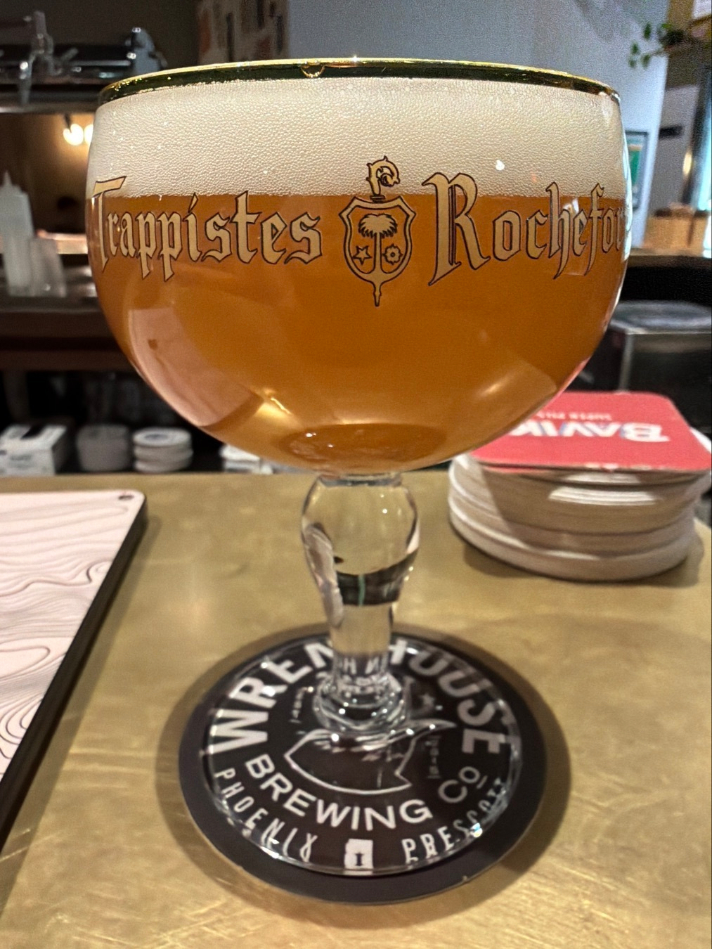 A glass of Trappistes Rochefort beer is placed on a bar counter, resting on a coaster.