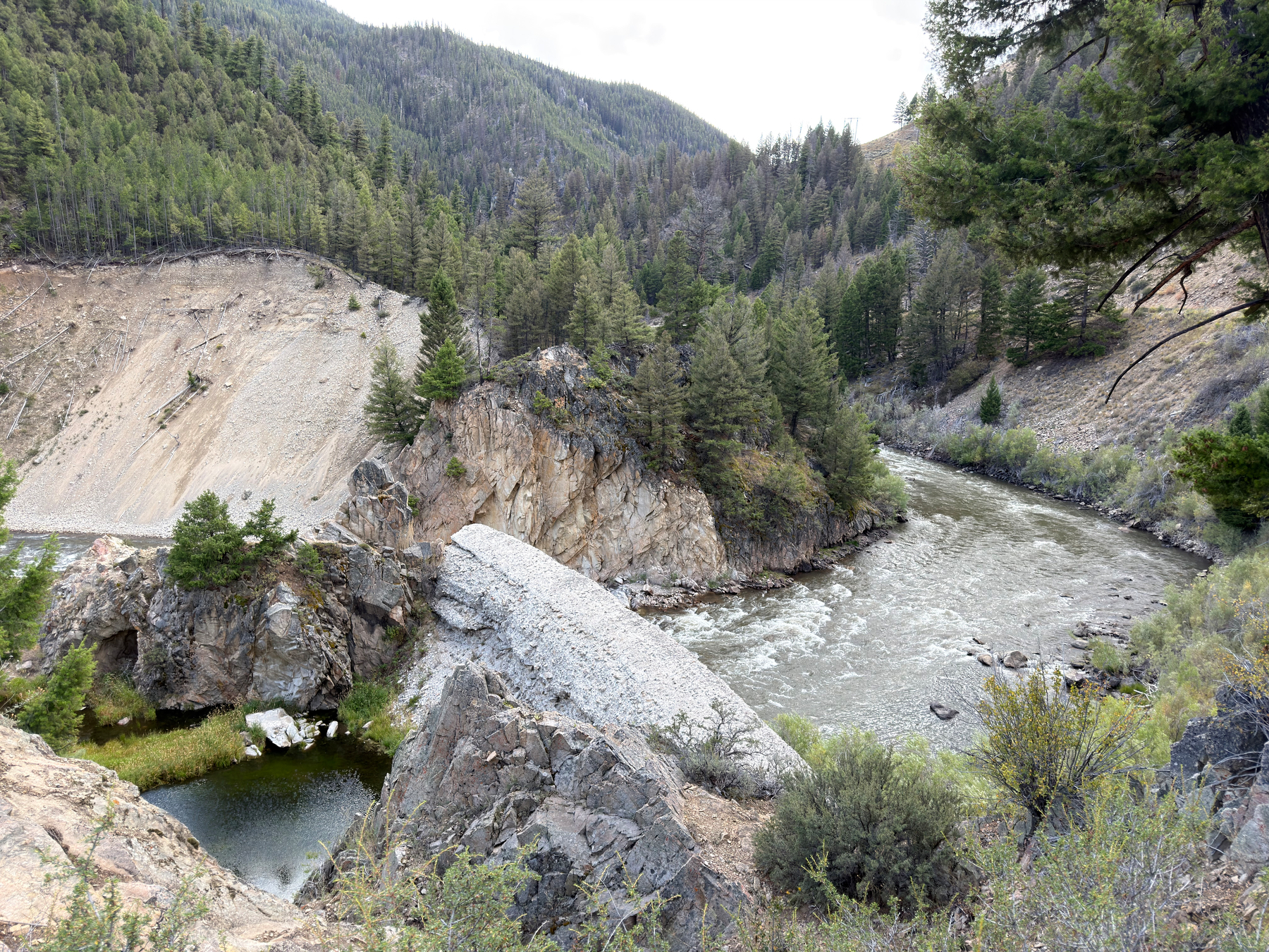 A natural rocky bridge spans across a river flowing through a forested mountainous area.