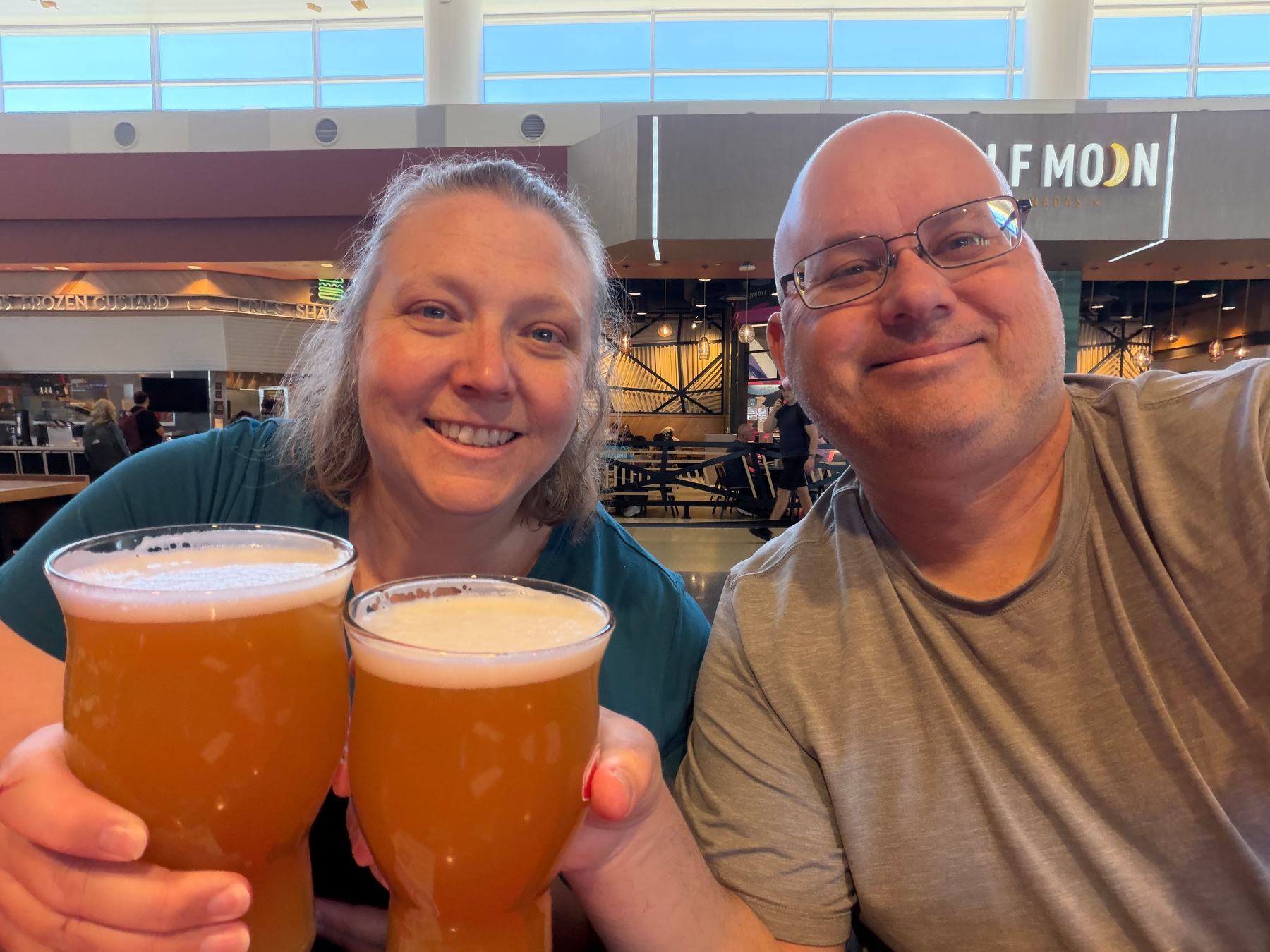 Two people are smiling and holding glasses of beer indoors.