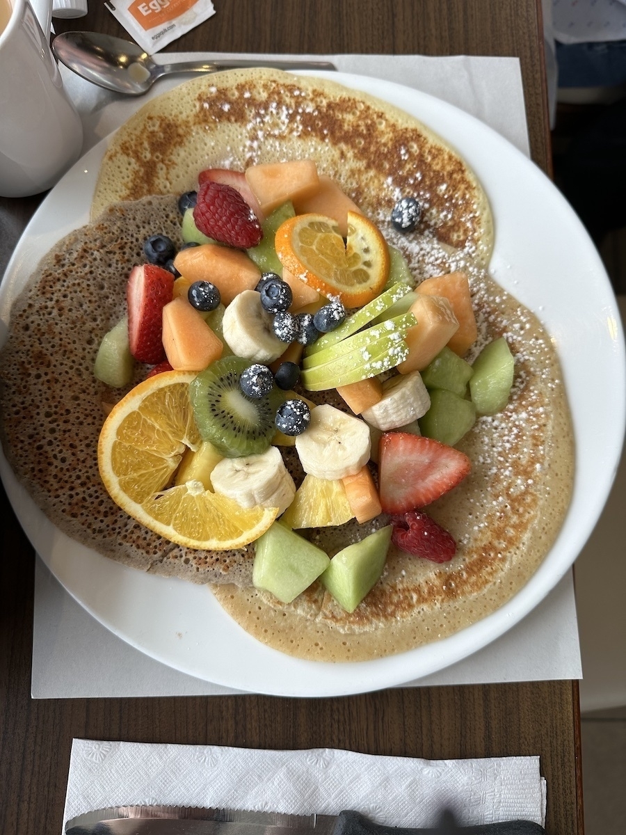 3 crepes on a plate piled high with fresh cut fruit