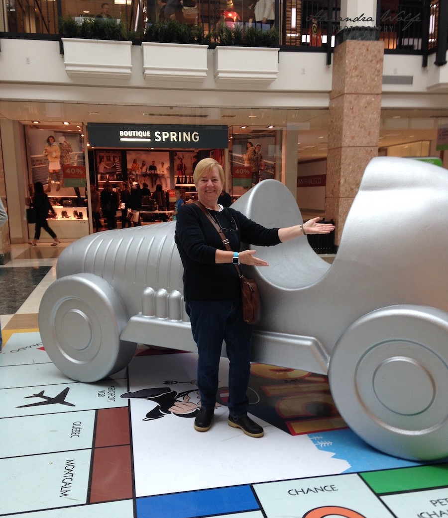 A person stands in front of a large Monopoly game piece replica shaped like a racecar in a shopping mall.