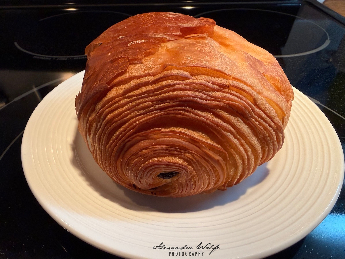 A flaky, golden-brown pastry, likely a pain au chocolat, rests on a white plate.