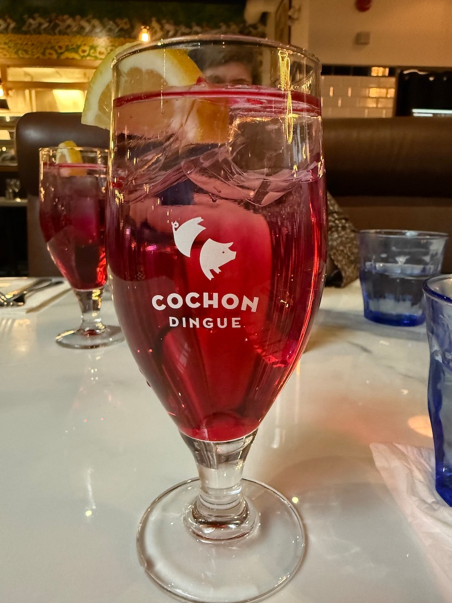 A glass of pink beverage with a lemon slice is served on a table, featuring the Cochon Dingue logo.
