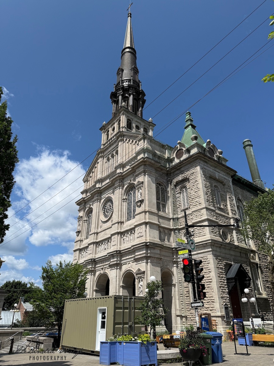 A tall, historic church with intricate stone architecture and a pointed spire stands against a clear blue sky.