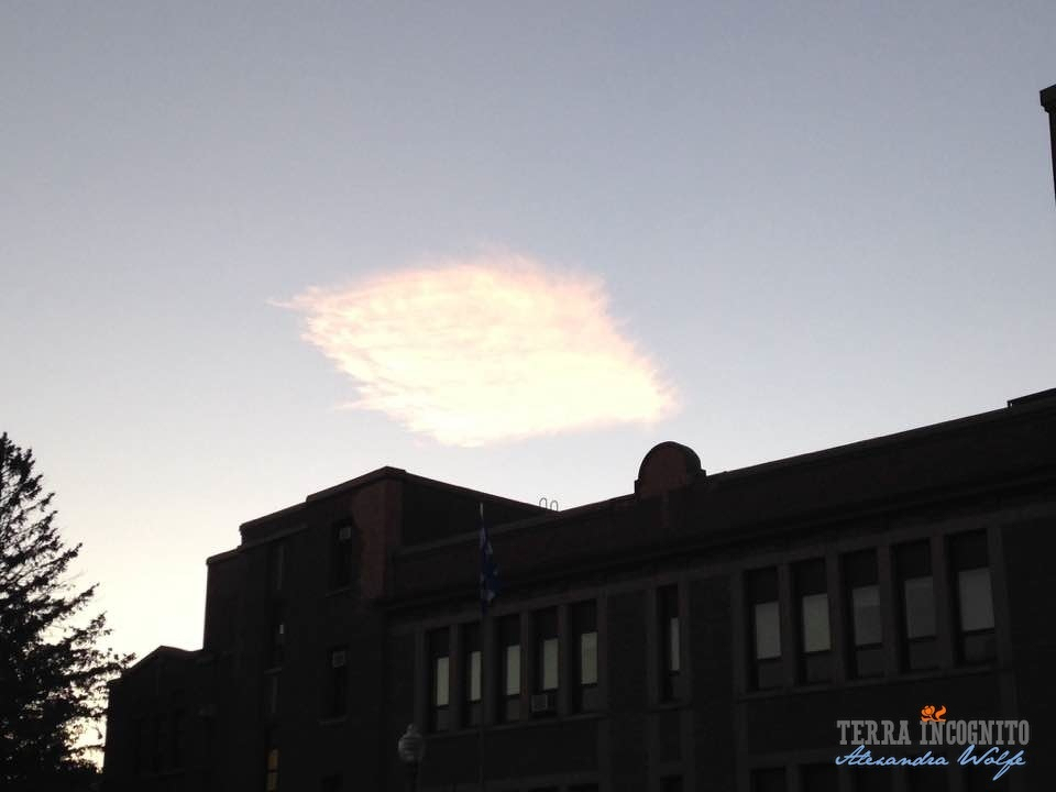 A bright, fluffy square-shaped cloud hovers over a silhouetted building at sunset.