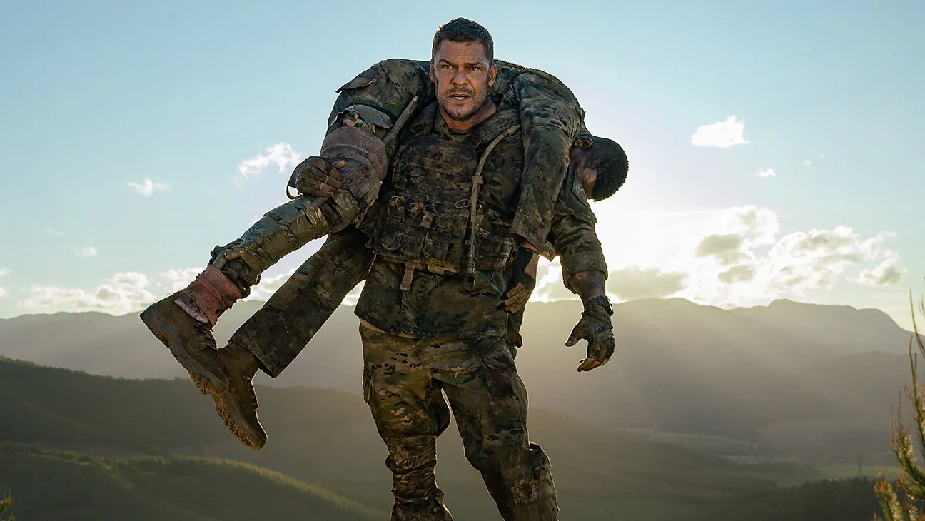 Auto-generated description: A soldier is carrying an injured comrade on his shoulders against a backdrop of mountains and a setting sun.