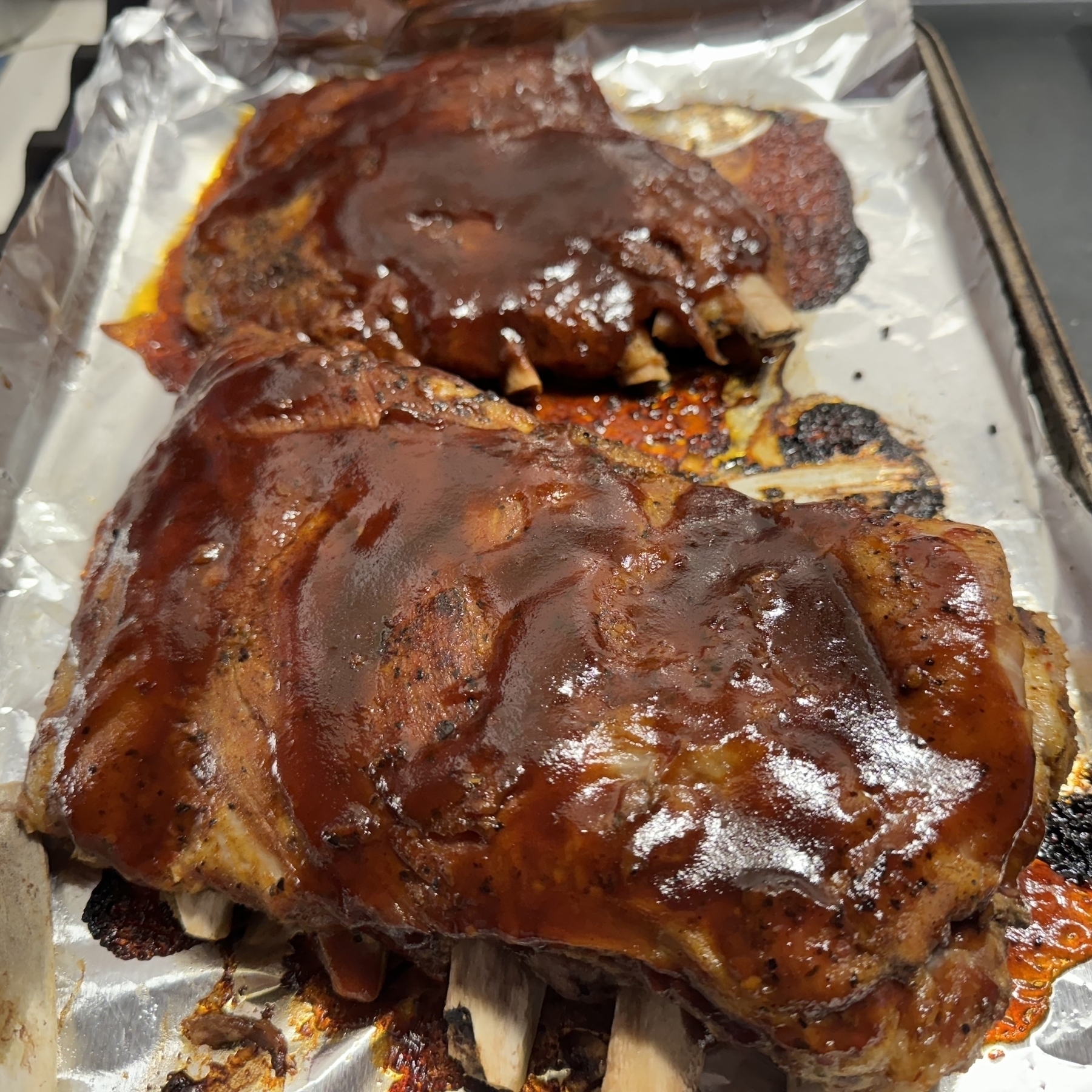 A cookie sheet loaded with enormous racks of ribs, thick with dark red barbecue sauce.