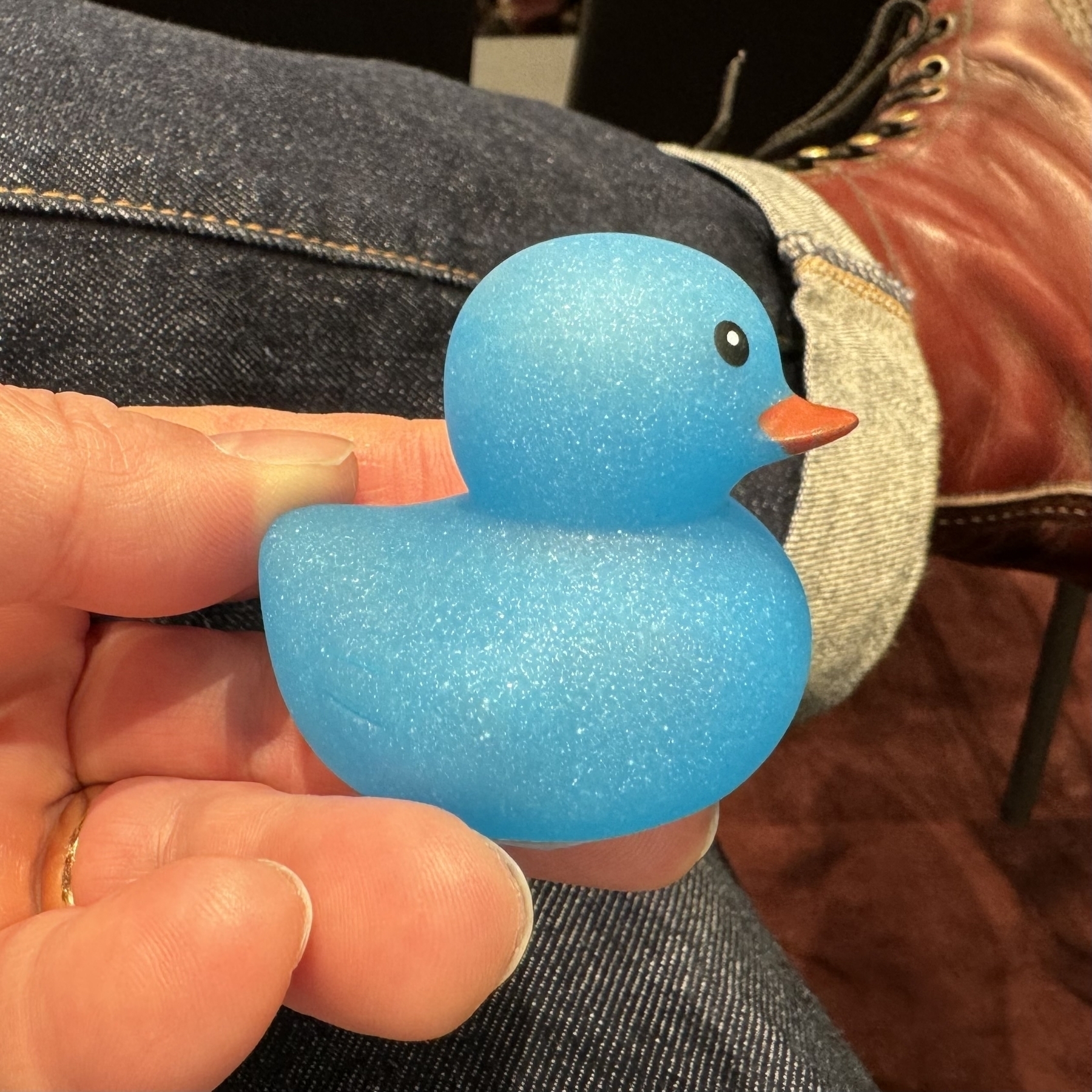 Someone is holding a small, metal flake blue rubber duck with an orange bill.