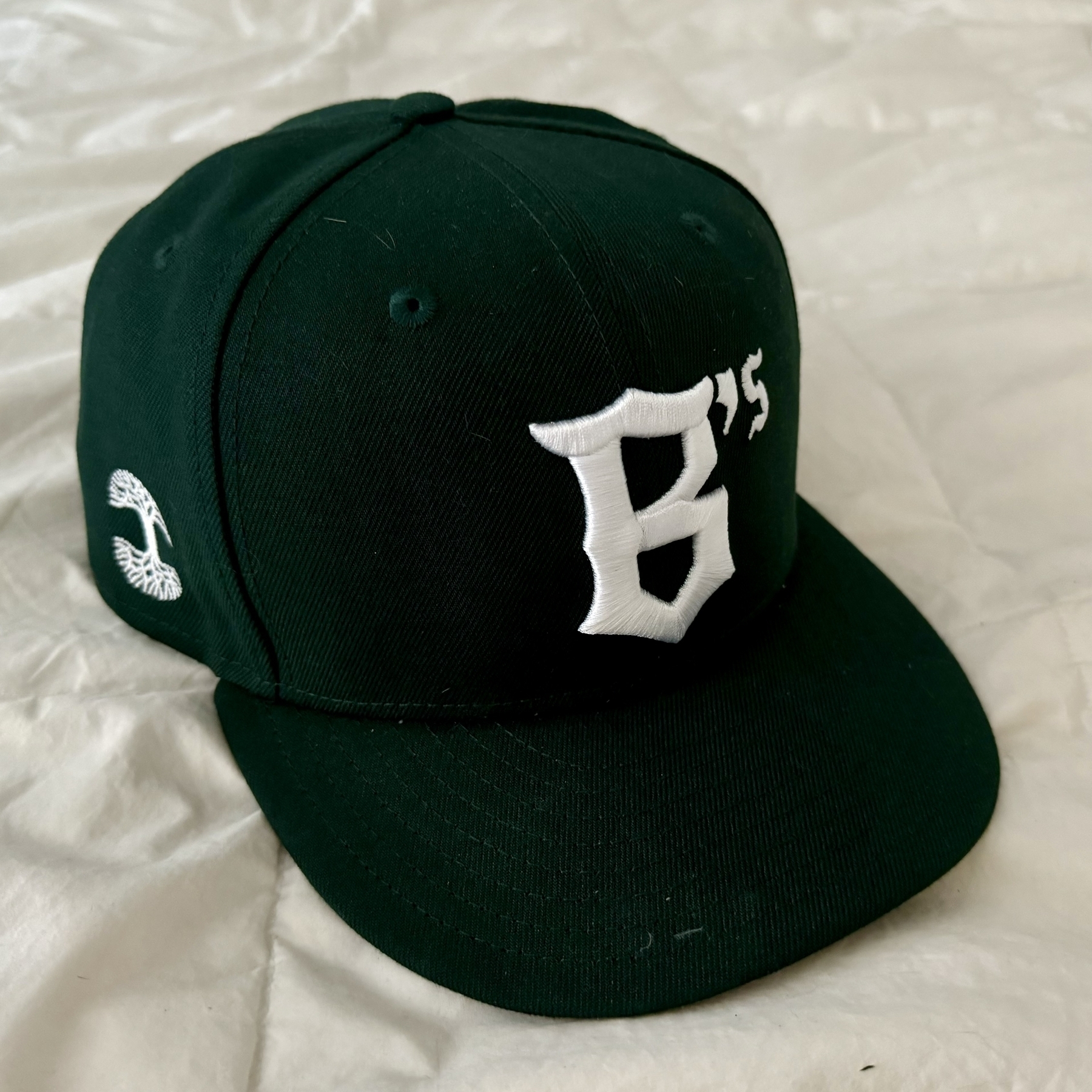 An Oakland B’s ballcap sitting on a white background. It’s dark green with a giant “B” on the front and the “Oaklandish” logo on the side. If you look closely, the opening in the bottom half of the B is shaped like the home plate of a baseball diamond.