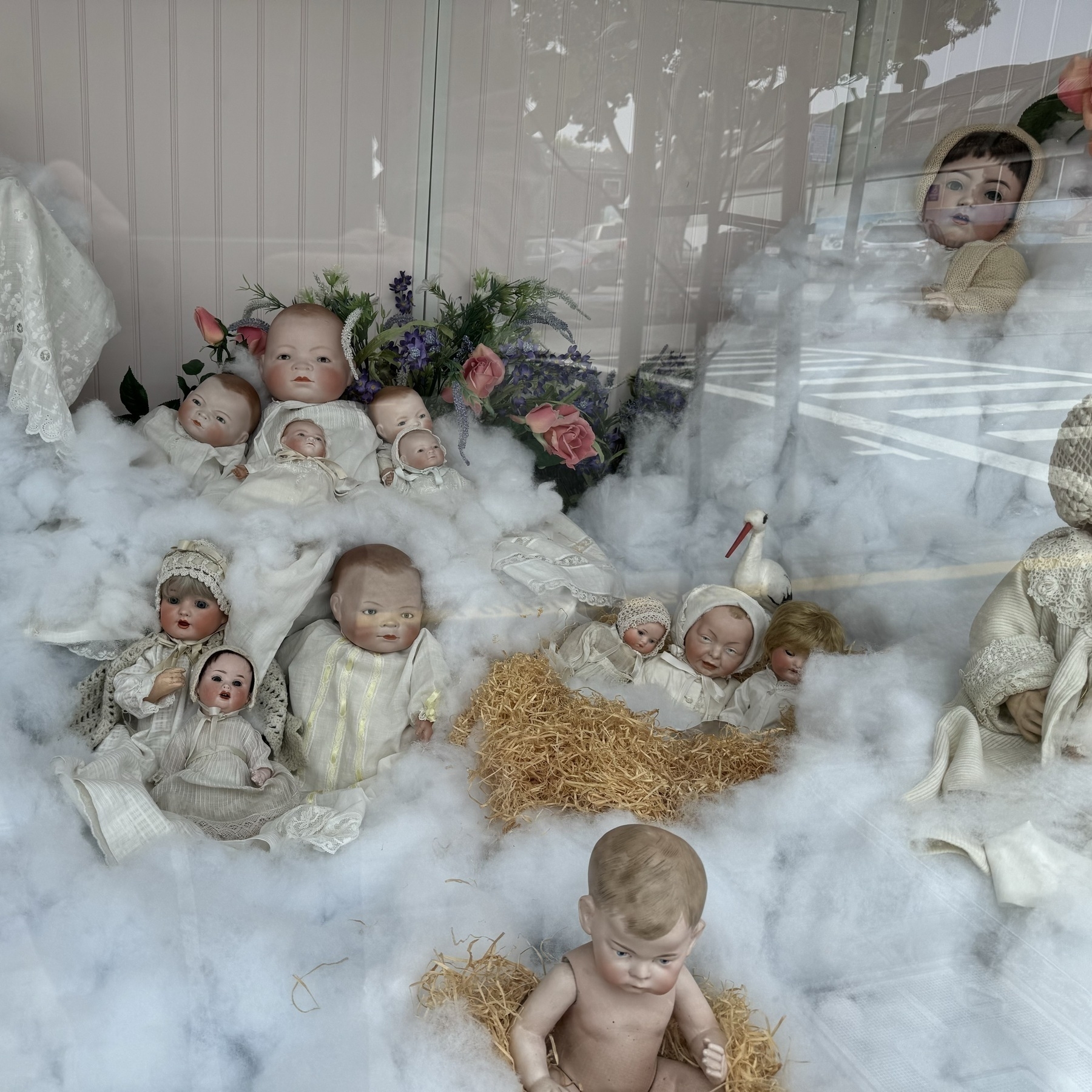 A store window is full of porcelain baby dolls sitting on cotton clouds. Many are dressed as angels. Their eyes look haunted. They can see you.