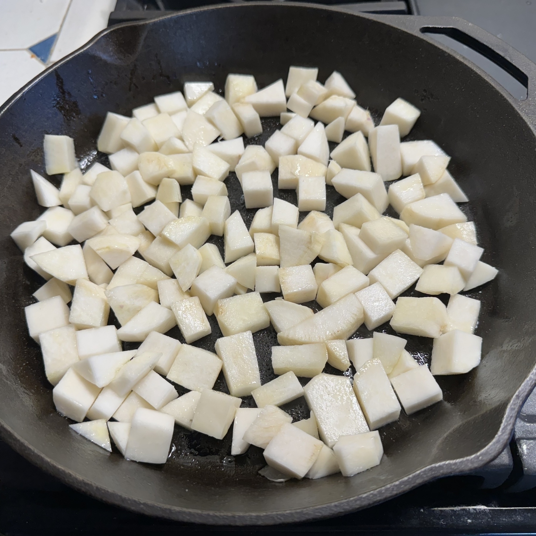 A cast iron skillet is lined with a layer of 1/2” cubed turnips, glistening in olive oil.