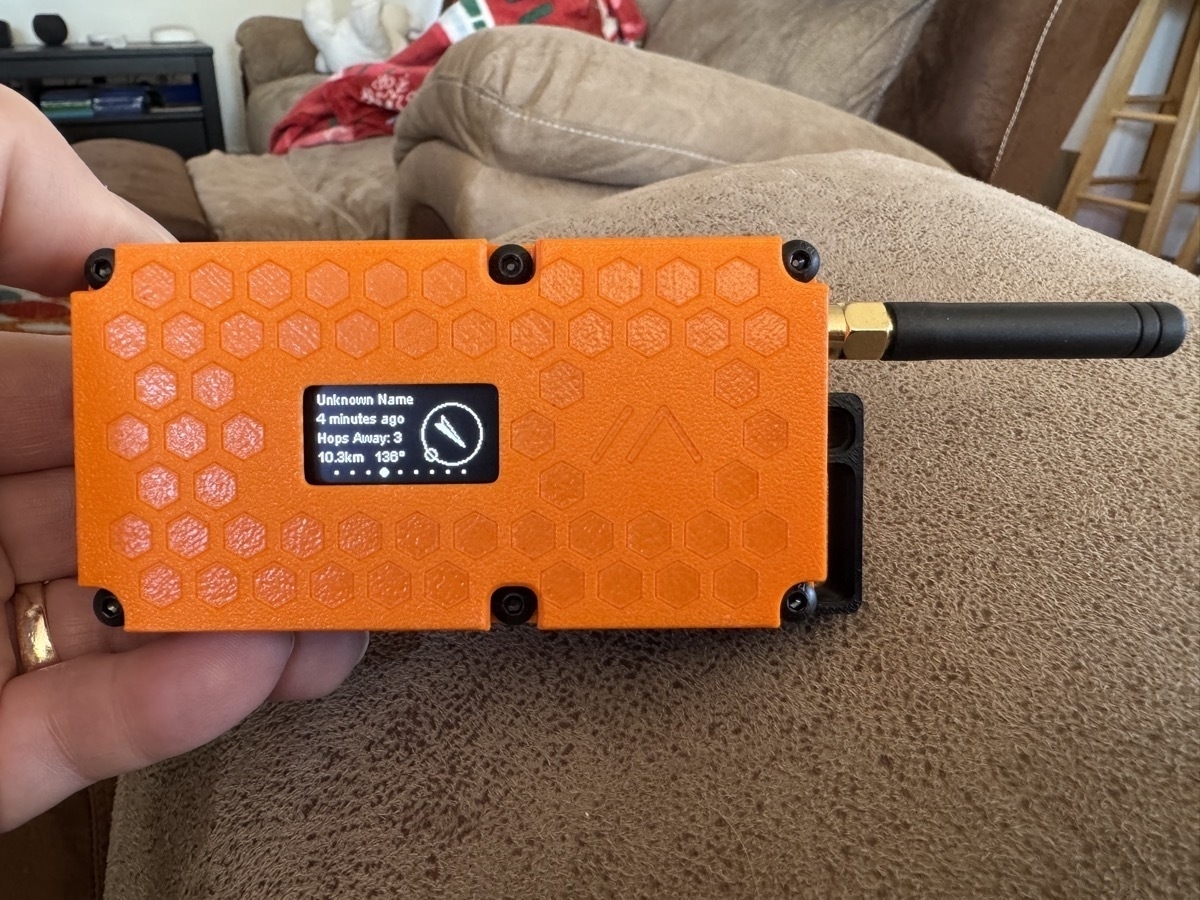 A rectangular orange Meshtastic RAK4631 case with an antenna off one corner, and an OLED screen in the middle.