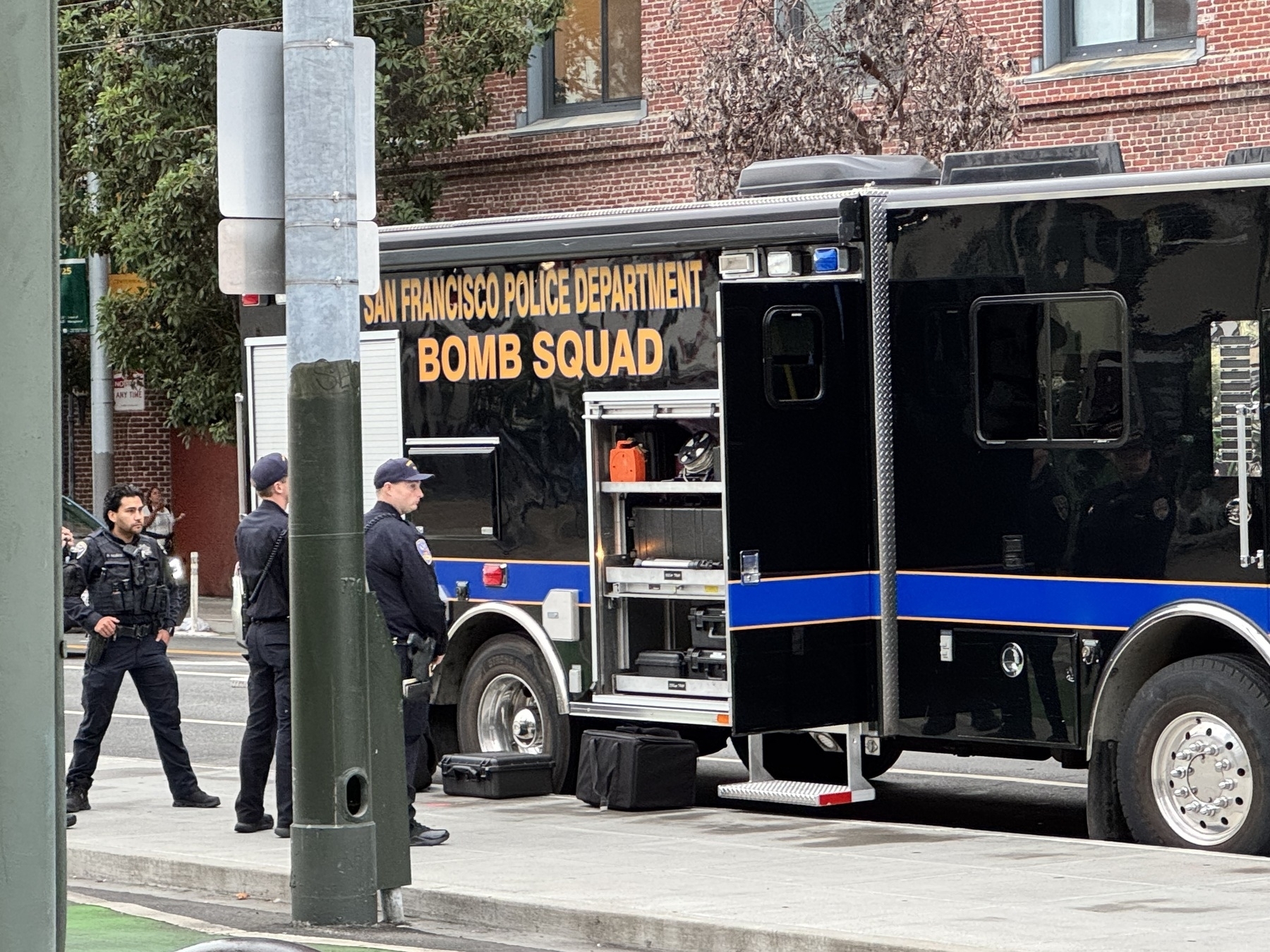 Armored police officers next to a large black truck labeled “San Francisco Police Department Bomb Squad”.
