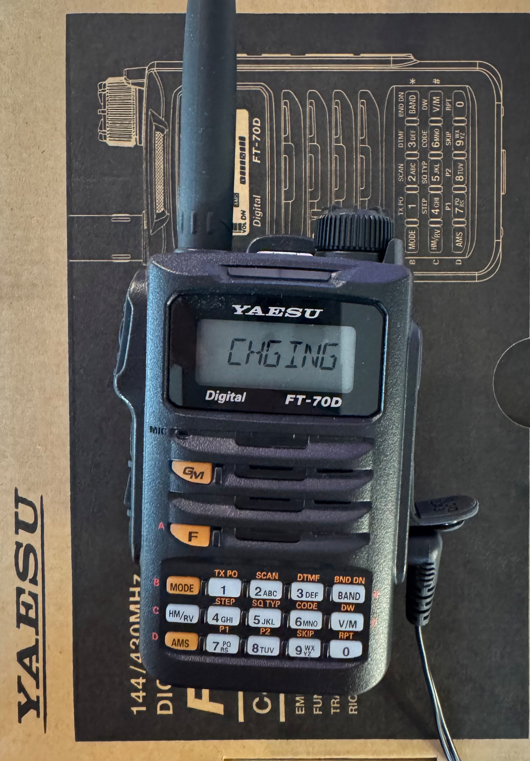 Photo of a Yaesu FT-70D sitting on its box and displaying a charging indicator.
