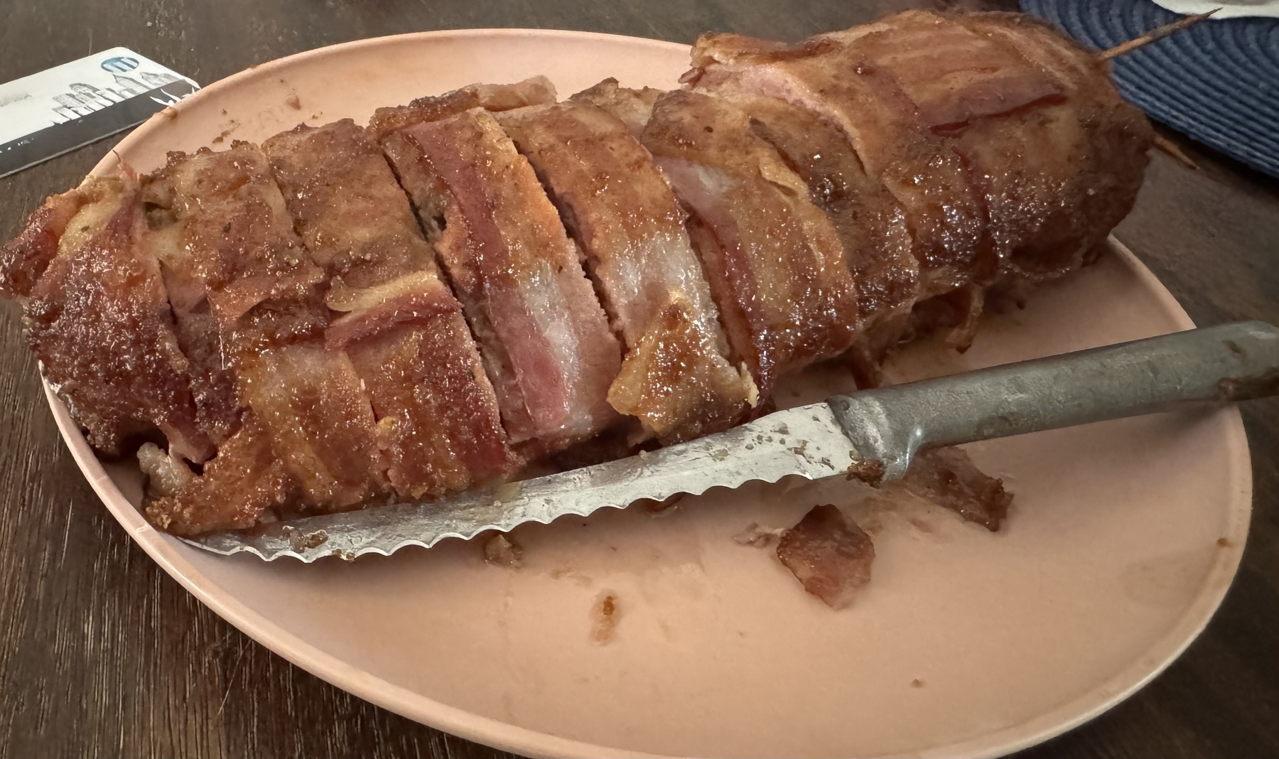 A plated breakfast fatty covers a platter. It’s dark brown an covered with laced bacon, and toothpicks hold it all together.