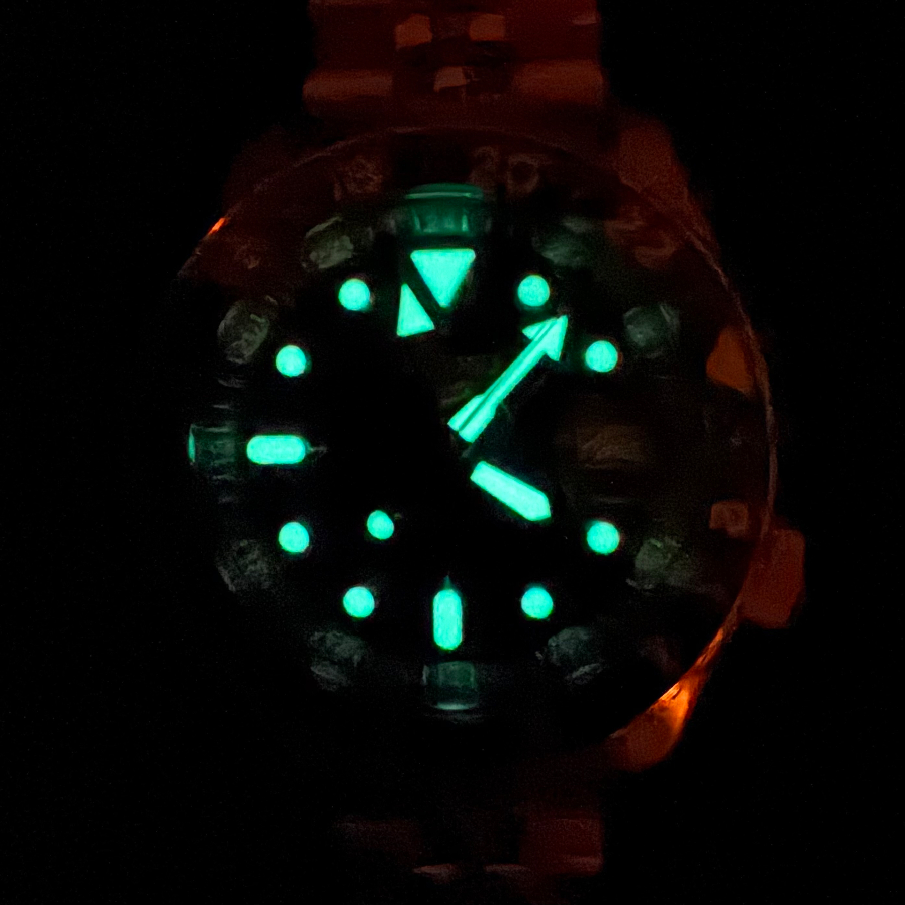 The same watch in a very dark room. Its hands and markings are glowing almost radioactively, brightly enough to read the numbers near them.