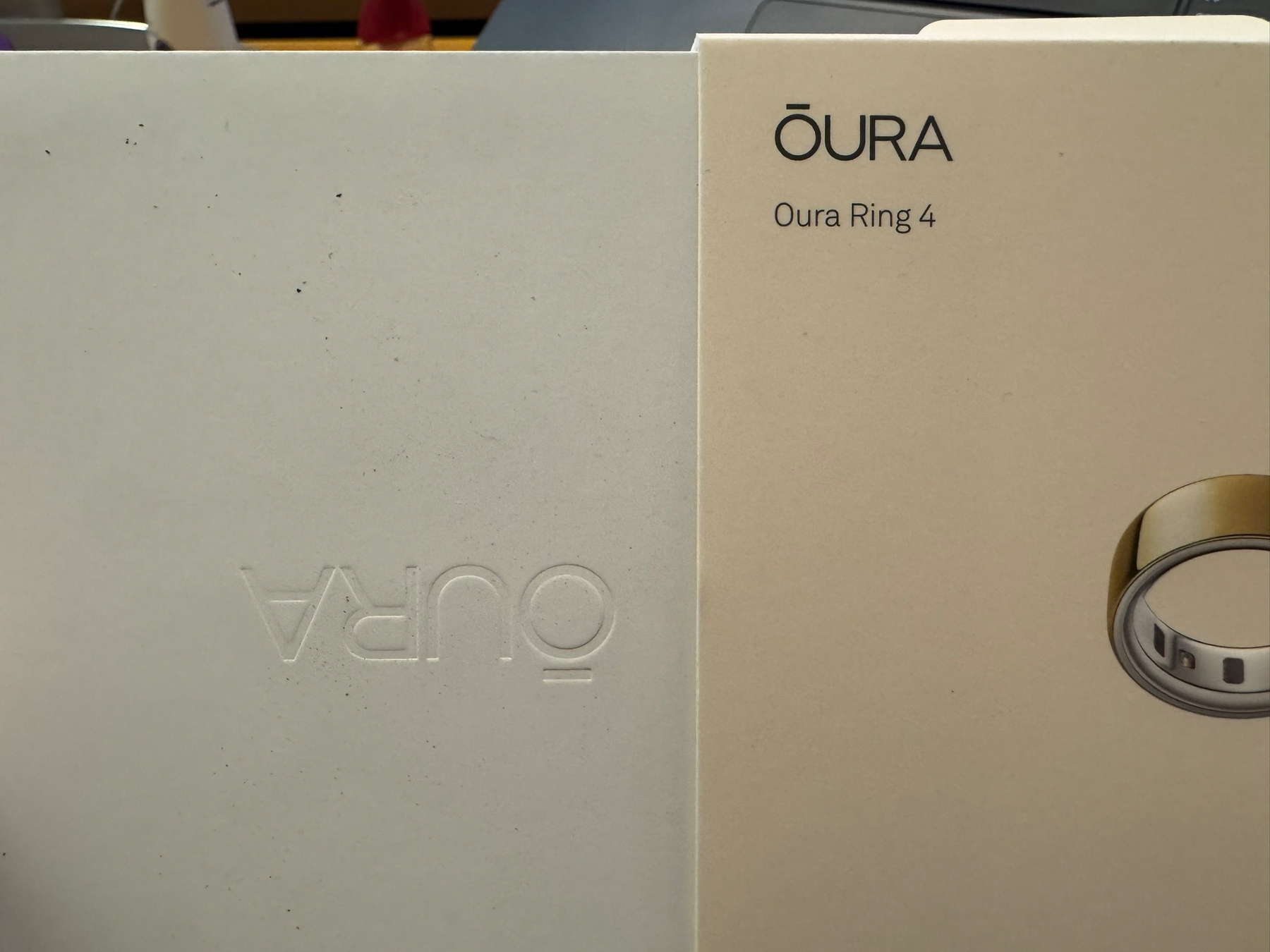 Photo of an Oura Ring box. The outside wrapper is right side up and readable. The inner box is partly out of that wrapper, and is rotated 180º so that its "Oura" embossing is upside down.