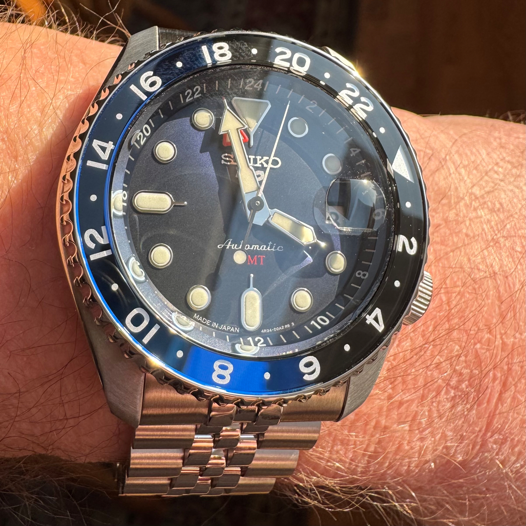 Closeup of someone wearing a Seiko SSK003 watch. The sun is shining on its face and reflecting the deep blue of the bezel.