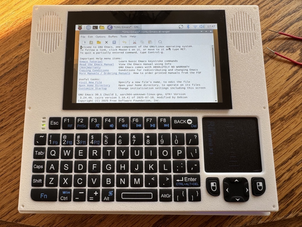 A 4.3 inch screen with a chiclet keyboard in a boxy white case displaying GNU Emacs on a GUI desktop.