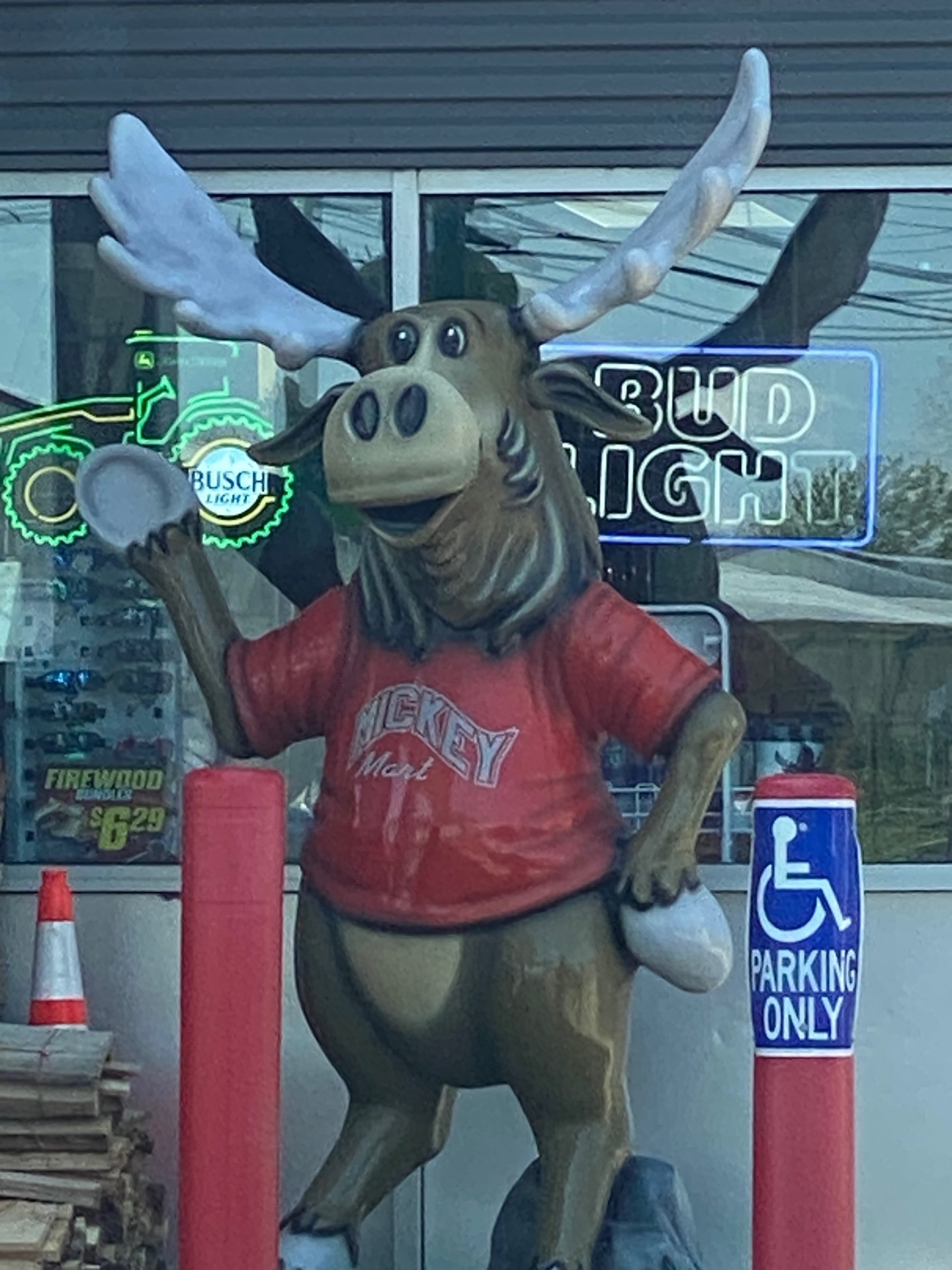 An anthromorphized moose statue in a red sweater smiling and waving outside of a gas station.
