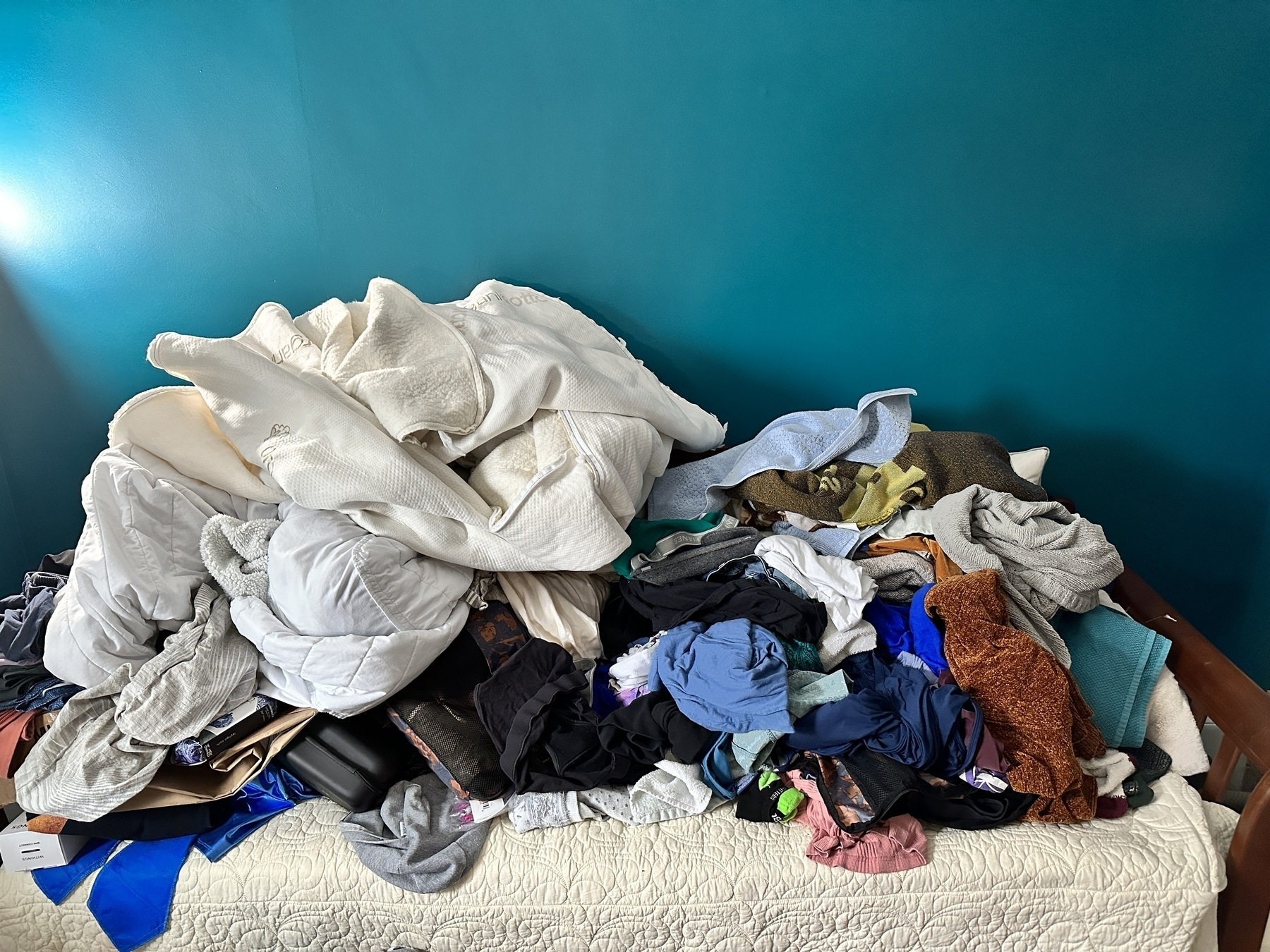 A giant, messy, unfolded pile of clothes and bedding hiding a daybed. 