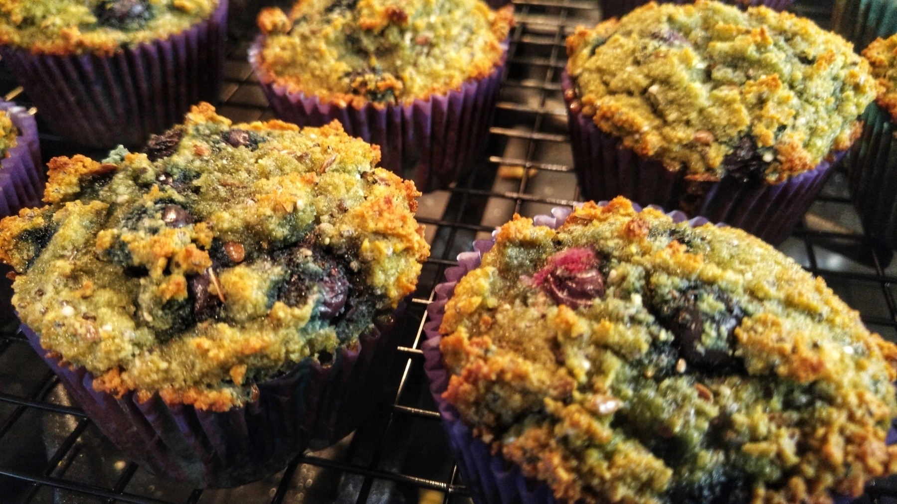 Full frame of freshly baked blueberry oat muffins in purple paper cups on a cooling rack. 