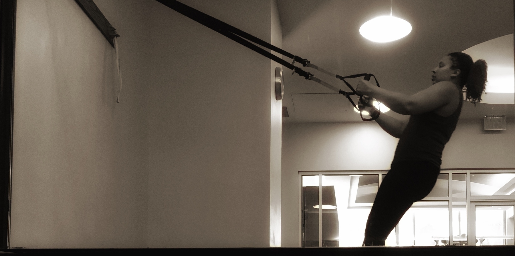B&W photo of a woman using a TRX system at a gym. 