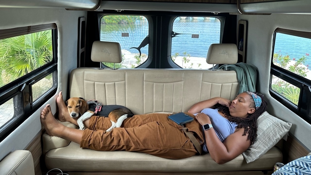 A brown woman laying on a lounge with a beagle resting on her feet. They both appear to be napping. 