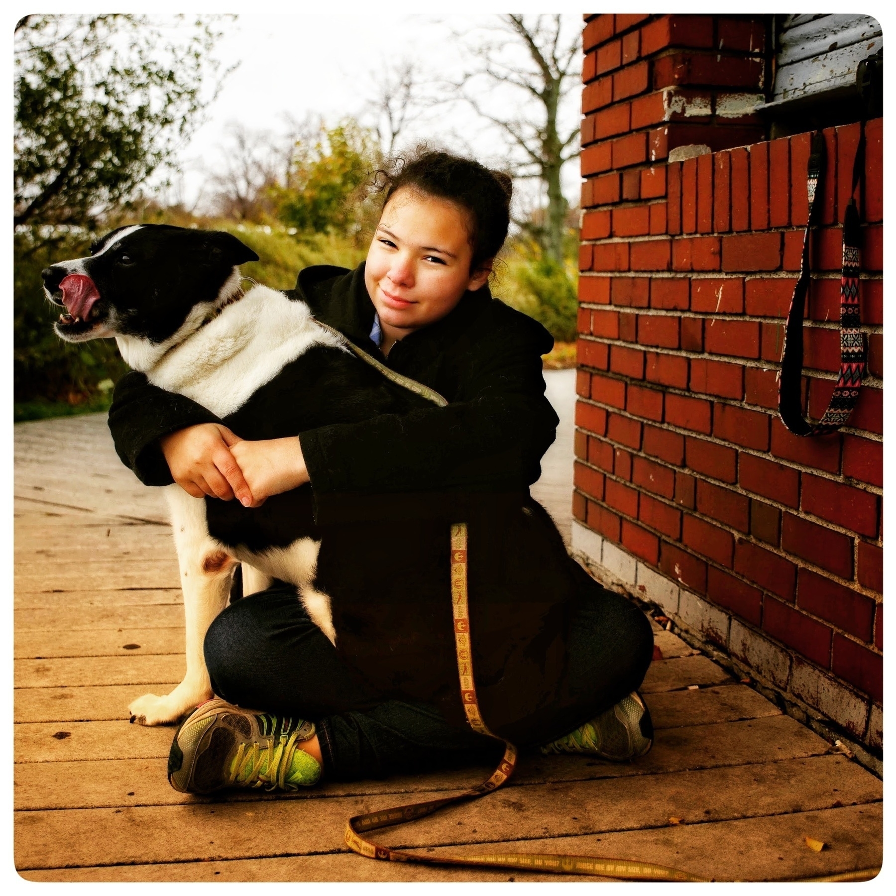 Young girl looking at the camera with her arms wrapped around a border collie that is looking off frame to the left. The collie has her tongue out. 