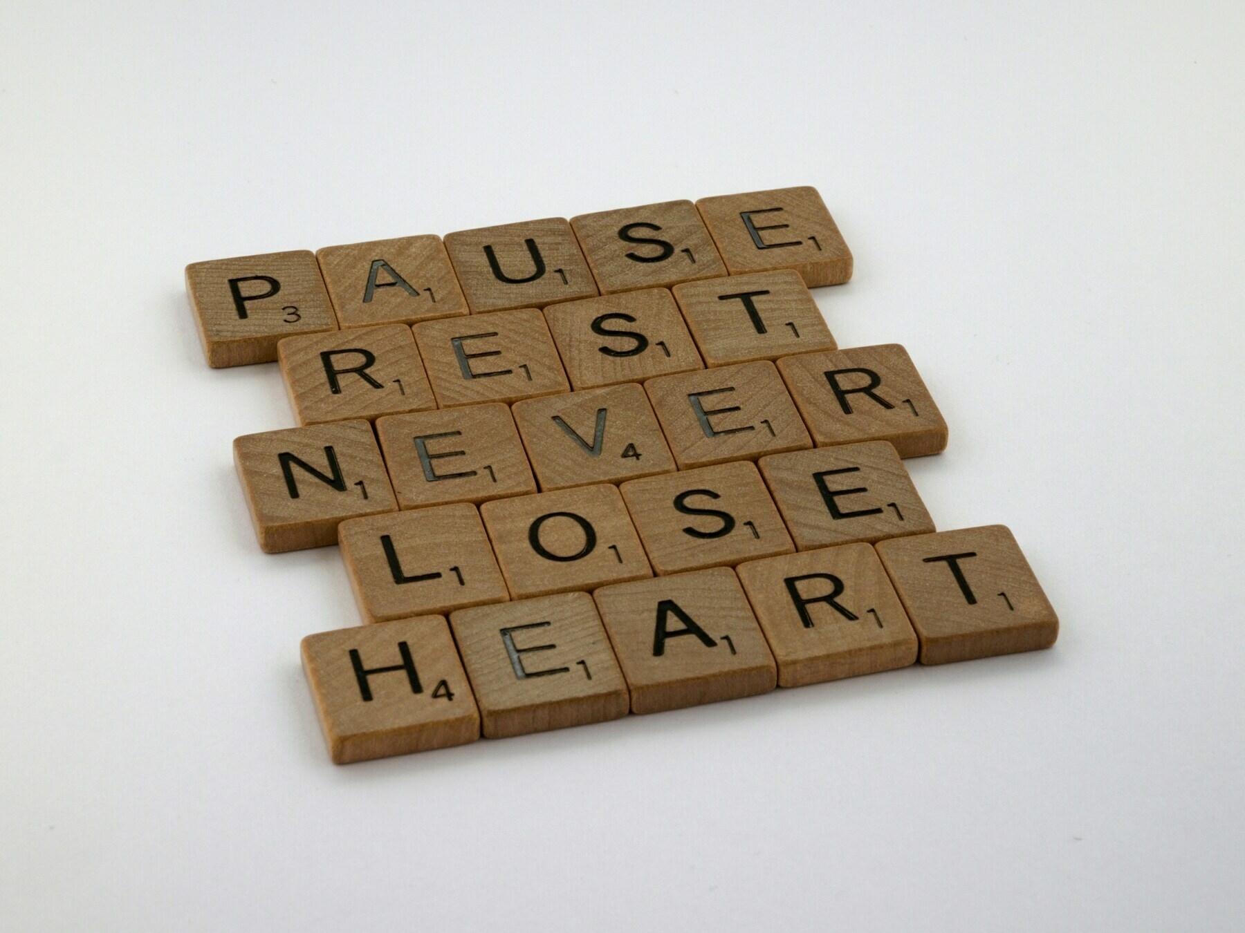 Brown wooden blocks stamped with letters reading: Pause | Rest | Never | Lose | Heart